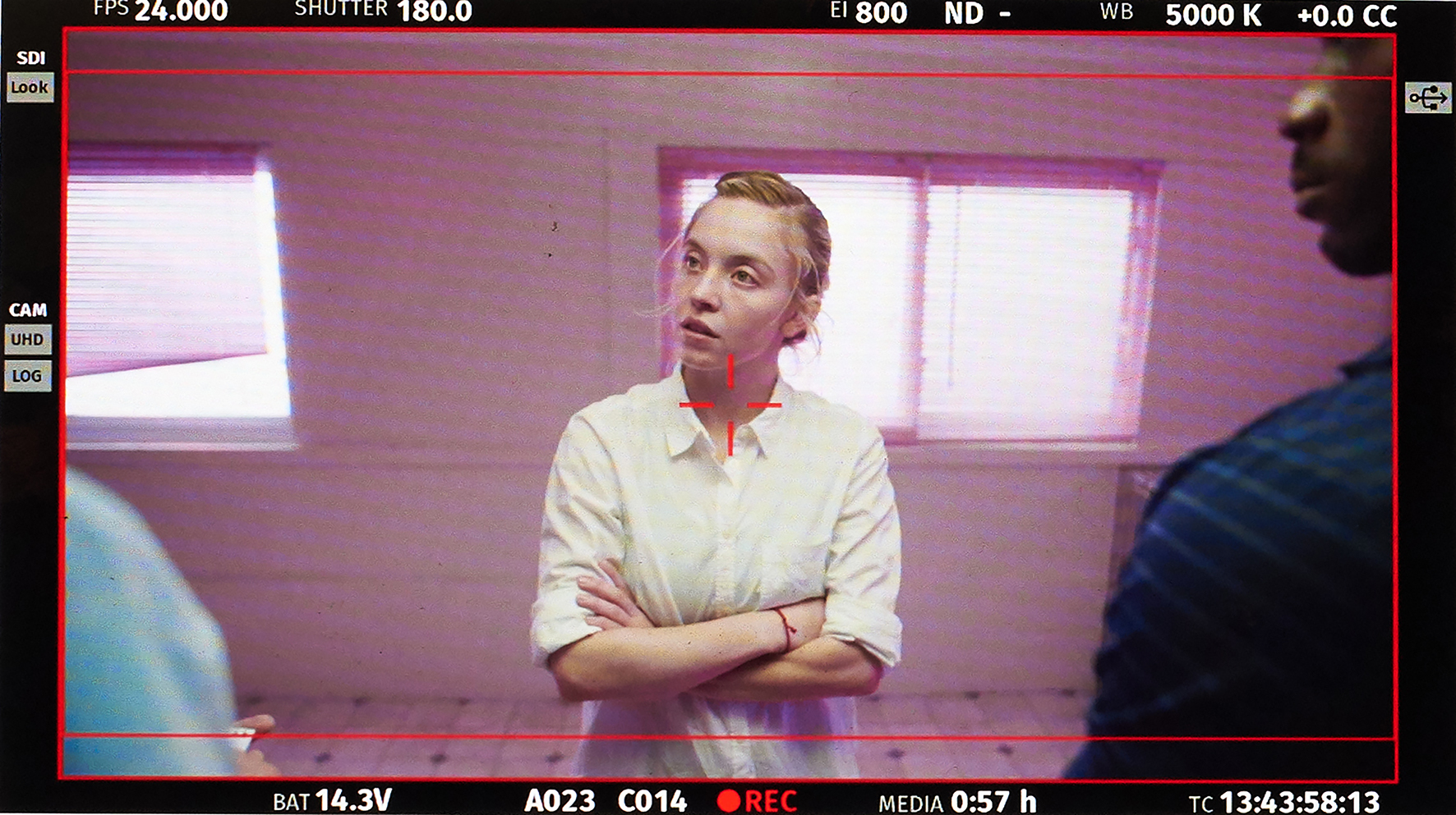 A woman swearing a white shirt stands with her arms crossed as she faces two men.