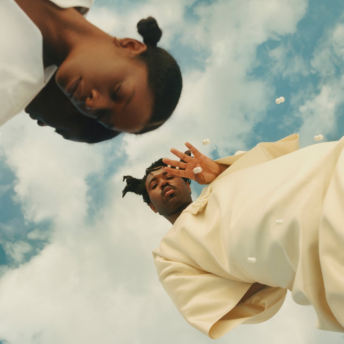Sampha wearing a white oufit, with a blue sky above him.