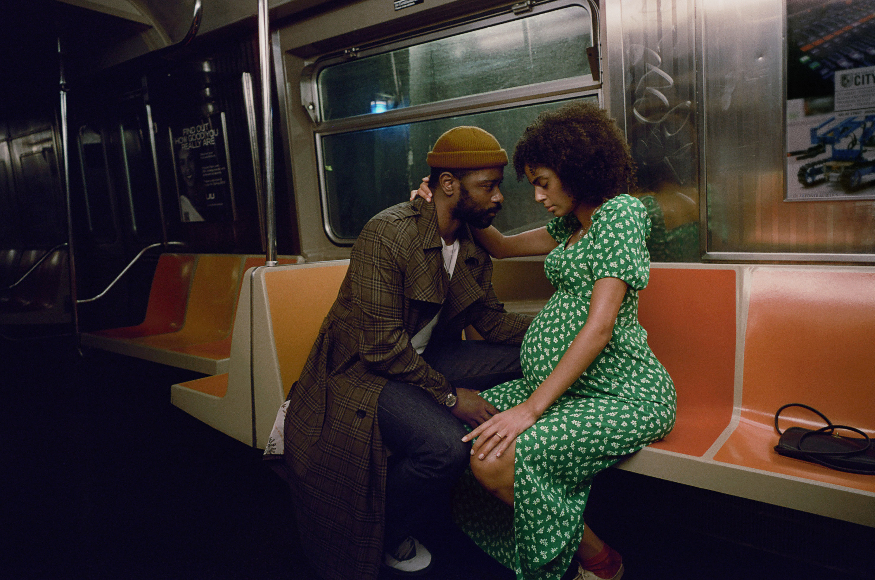 A man sits with a pregnant woman on a subway train.