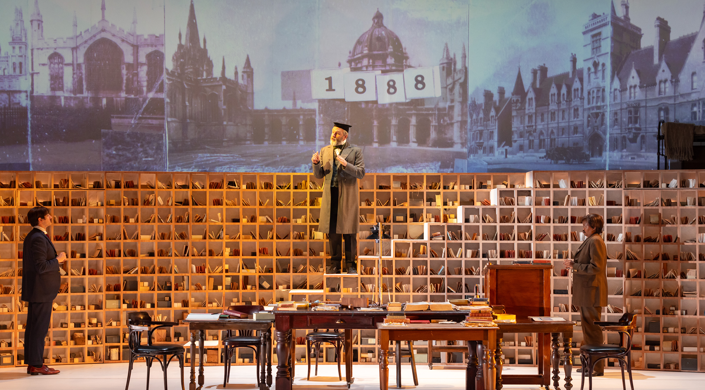 A professor stands atop a bookshelf.