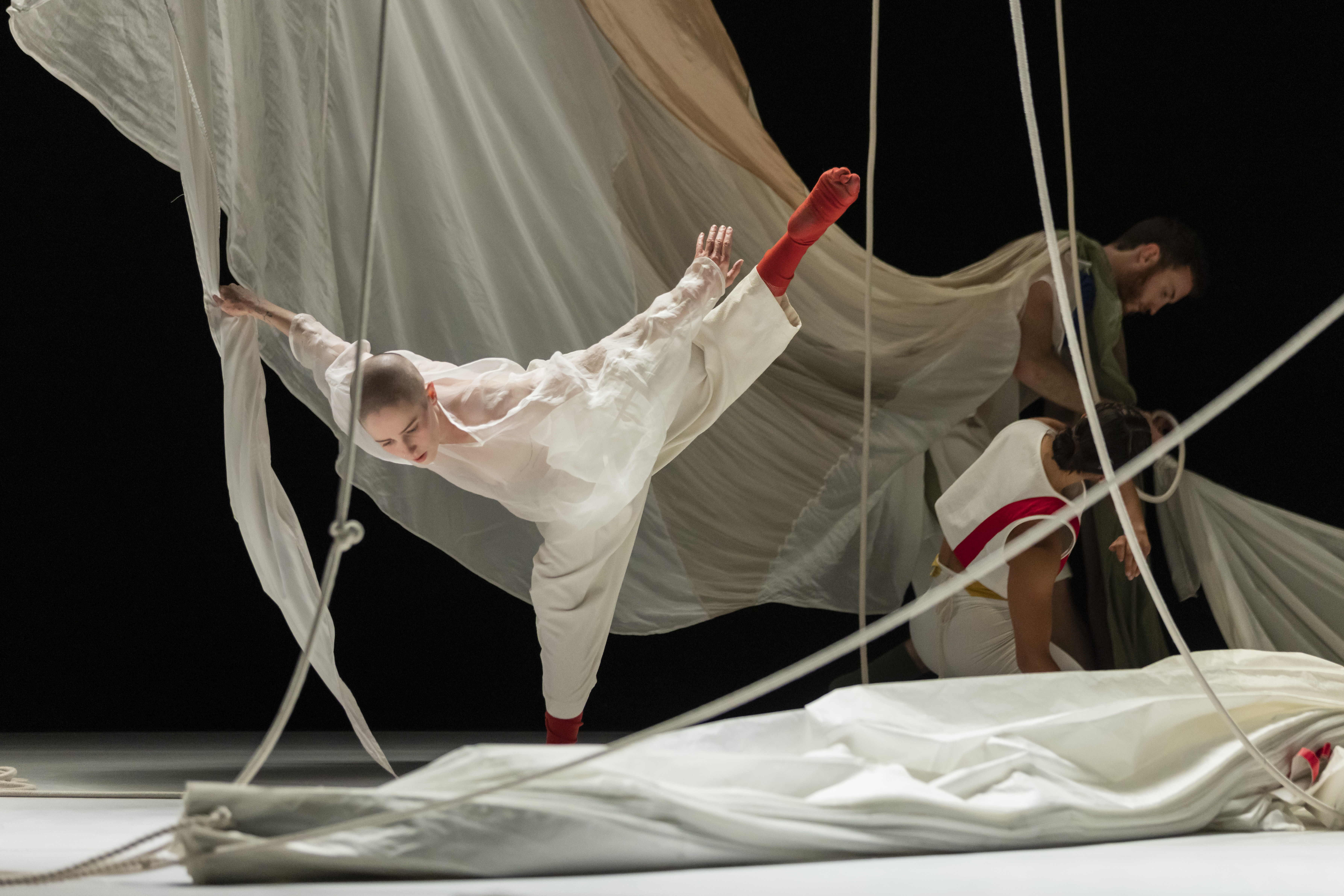 A dancer performers in a white outfit with sheets draped around them.