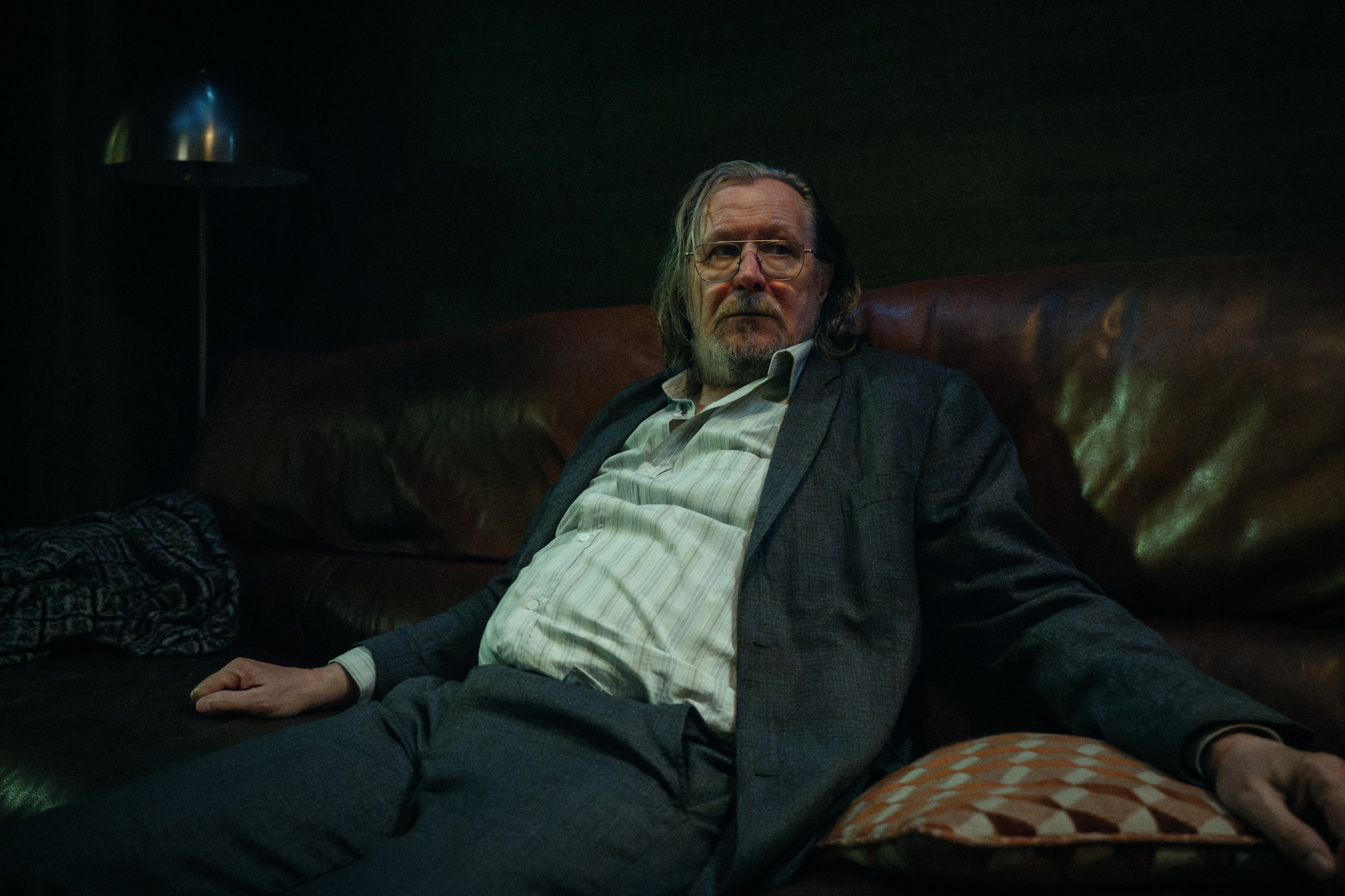 Gary Oldman slouched on a couch.