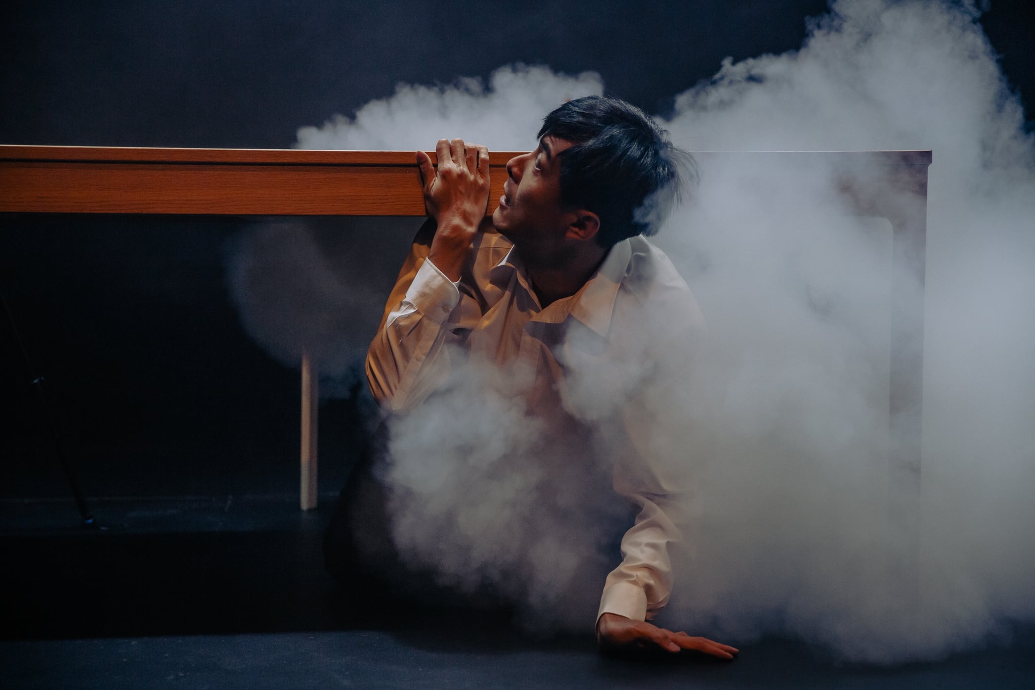 Wang Chong on stage, hiding under a desk as smoke fills the room.