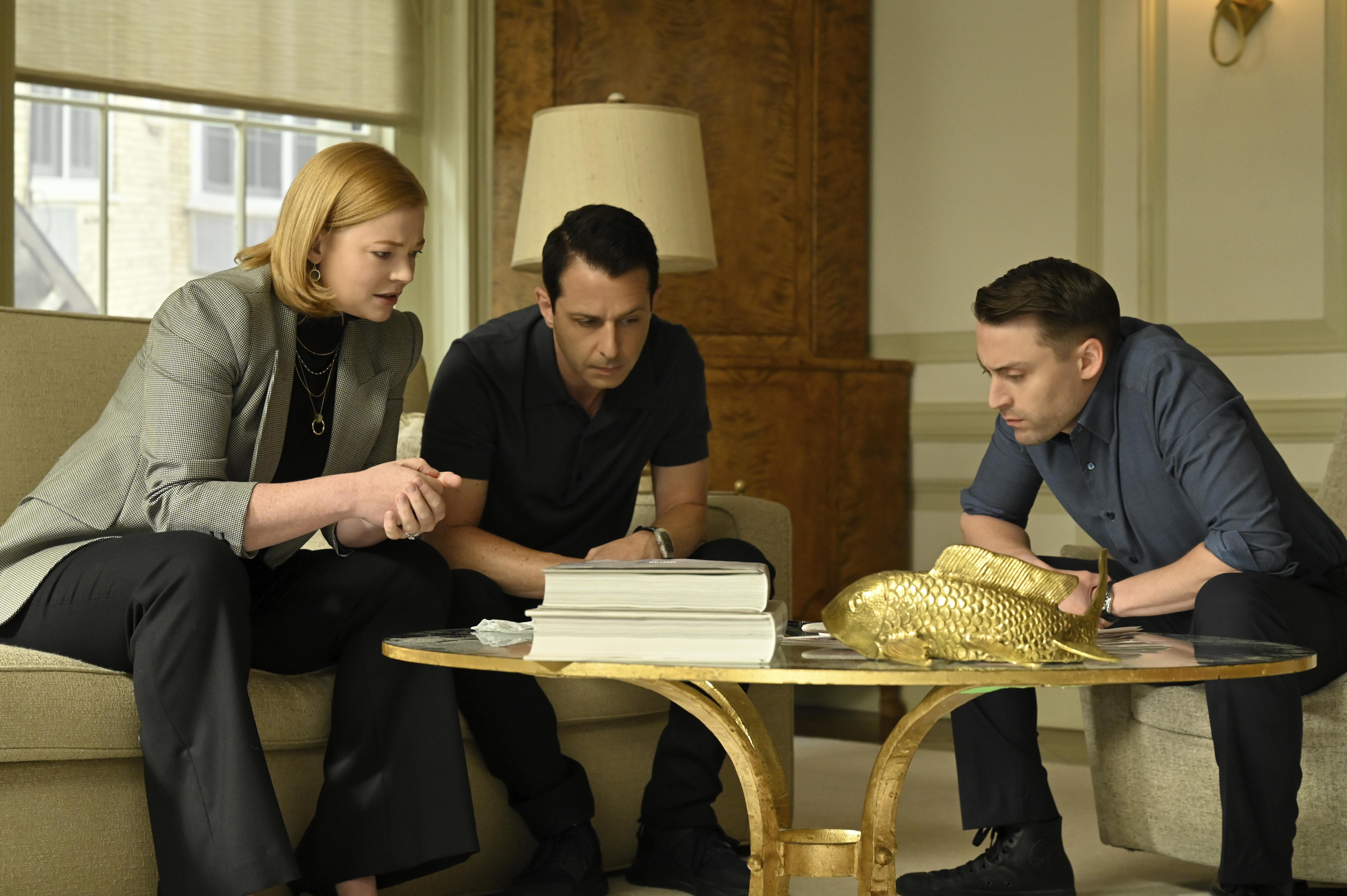The three siblings of Succession sit on armchairs, leaned toward each other in  conversation.