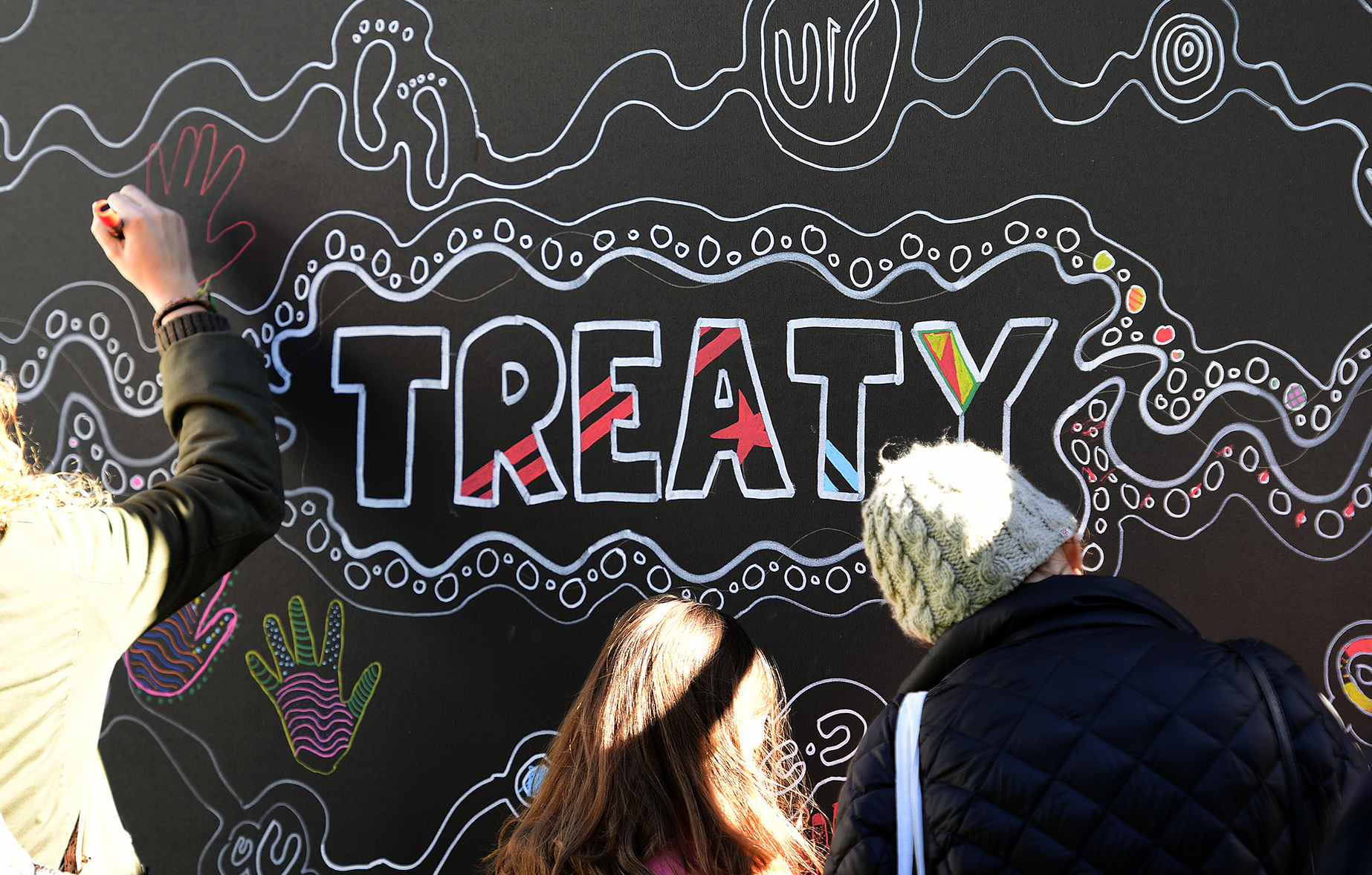 People draw “TREATY” on a communal art board.