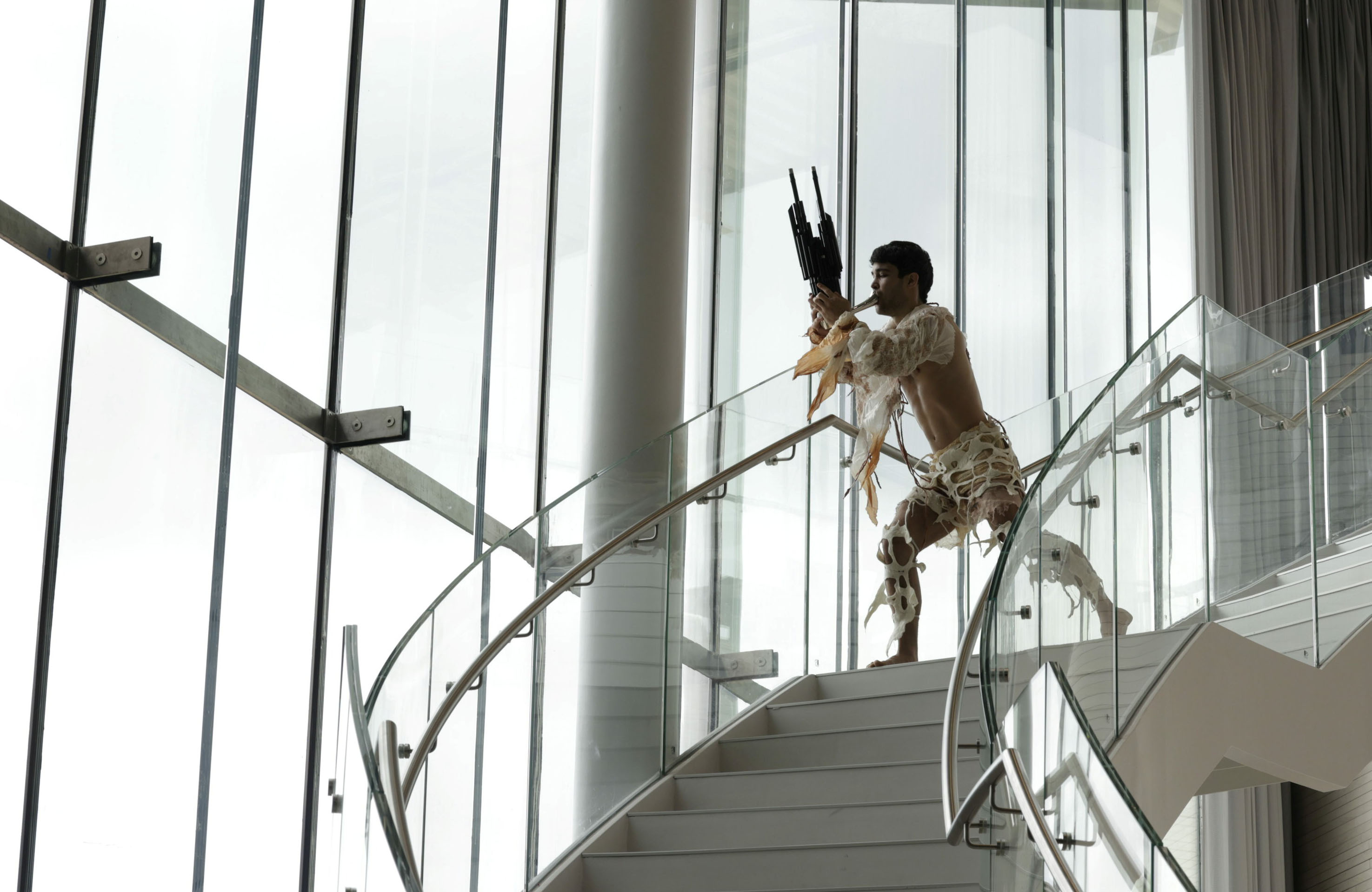 A performer blowing into an instrument on a spiral staircase.