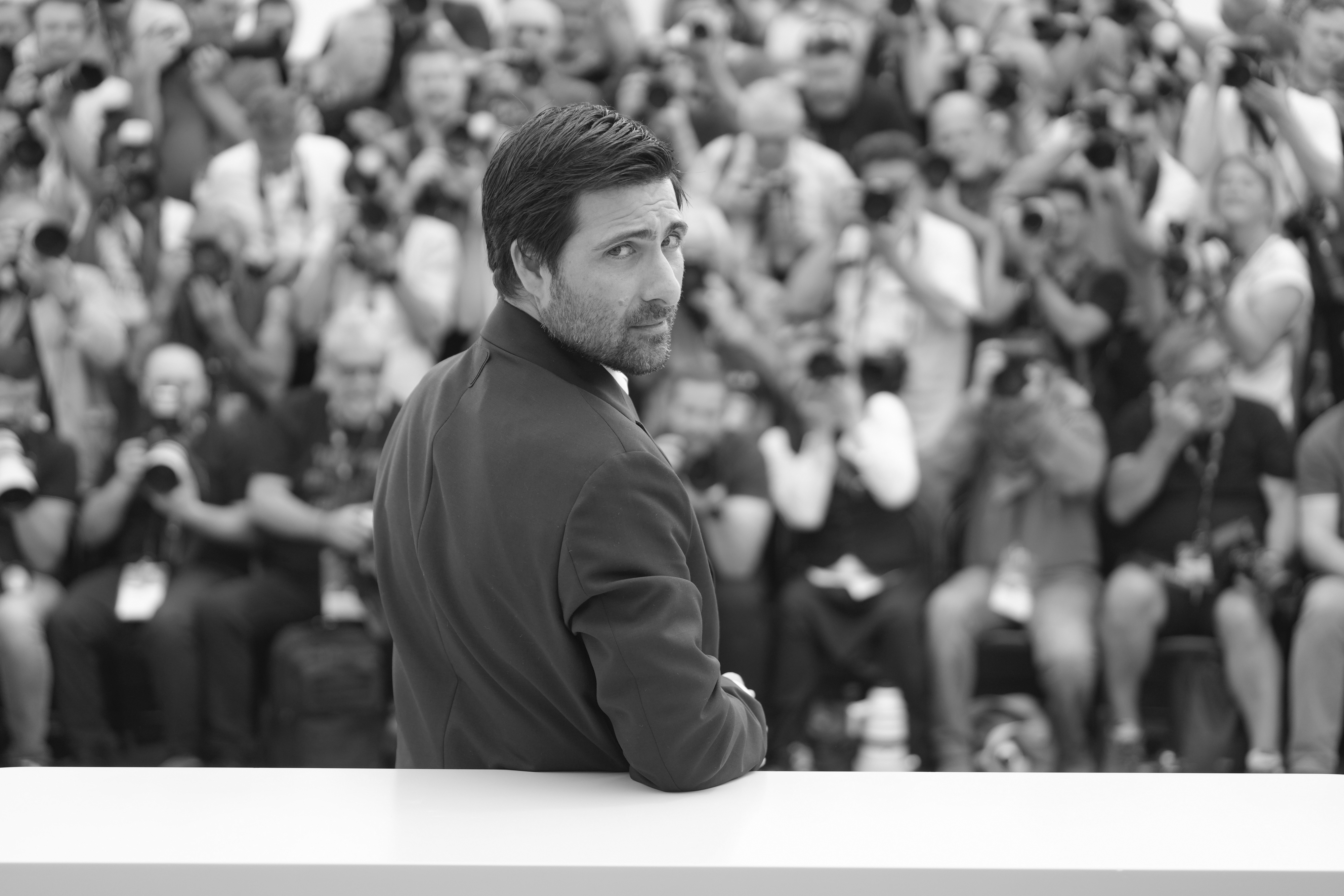 A man in a suit looks behind him as a crowd of photographers take his picture.