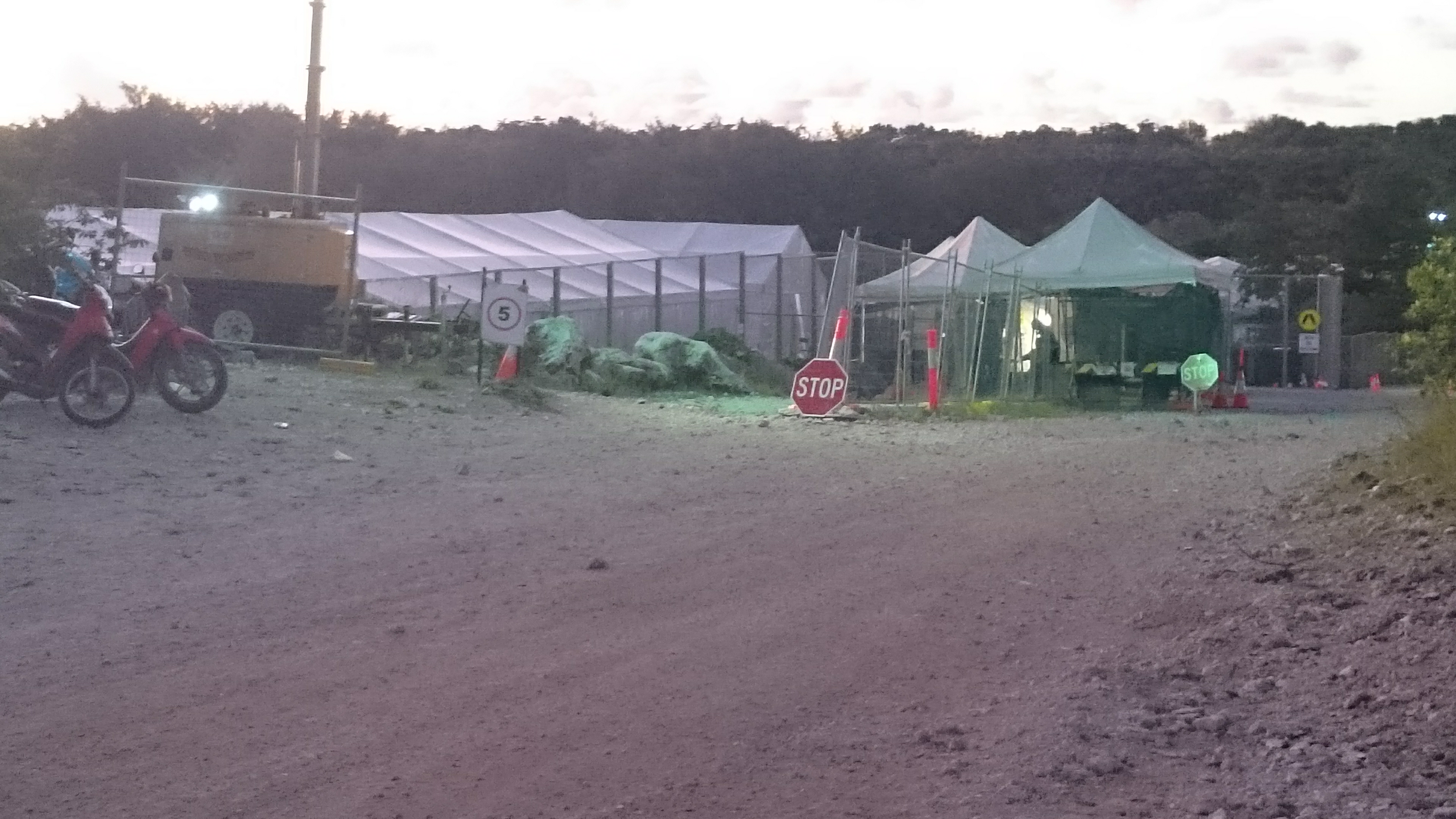 A gravel road with a detention centre in the distance.