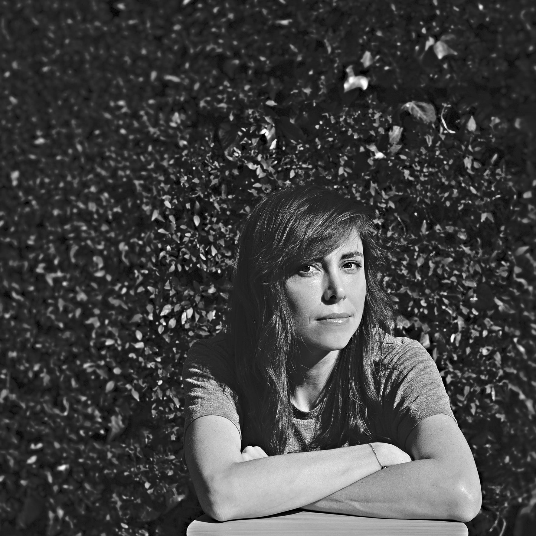 A woman poses for a portrait photograph with a hedge in the background.