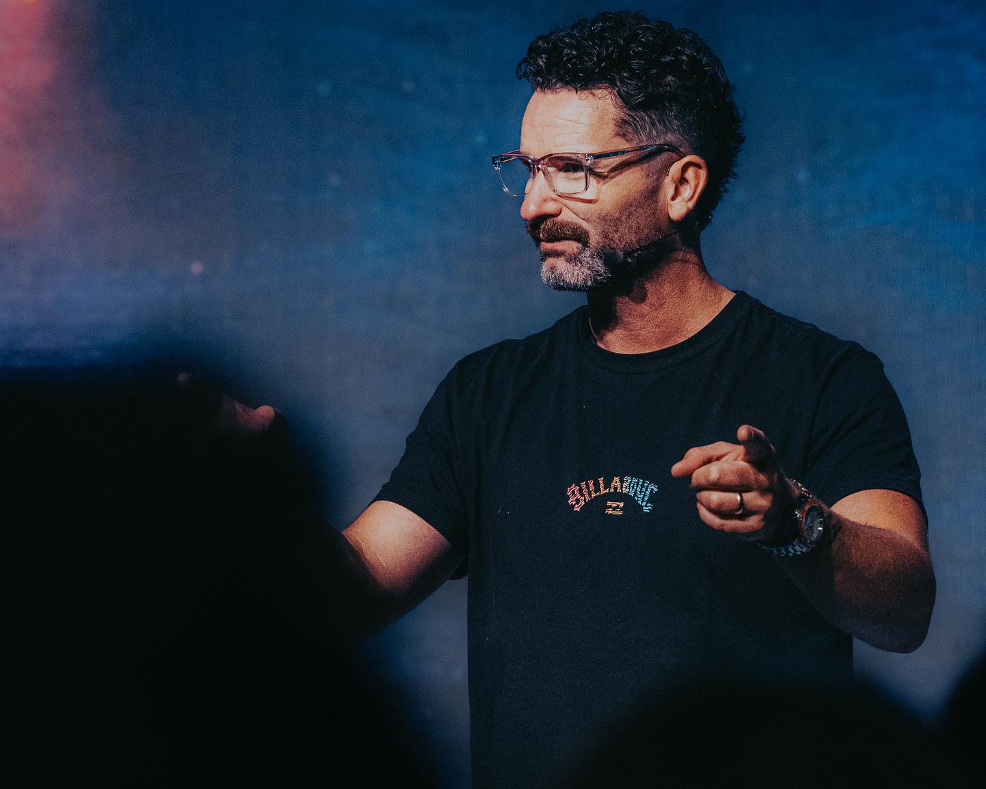 A mean wearing glasses speaks to a crowd with his hands raised.