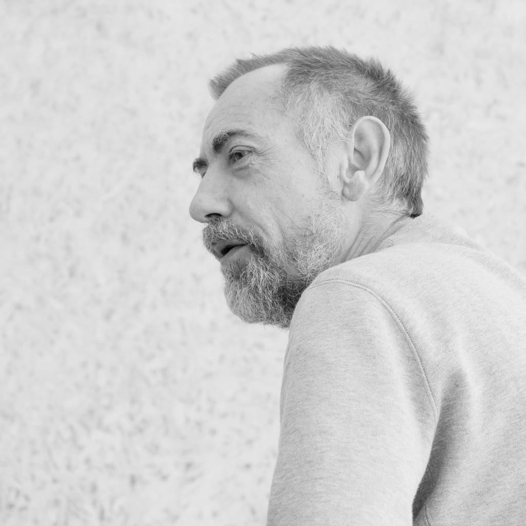 Portrait photograph of John Warwicker. He wears a grey beard matched with a grey jumper.