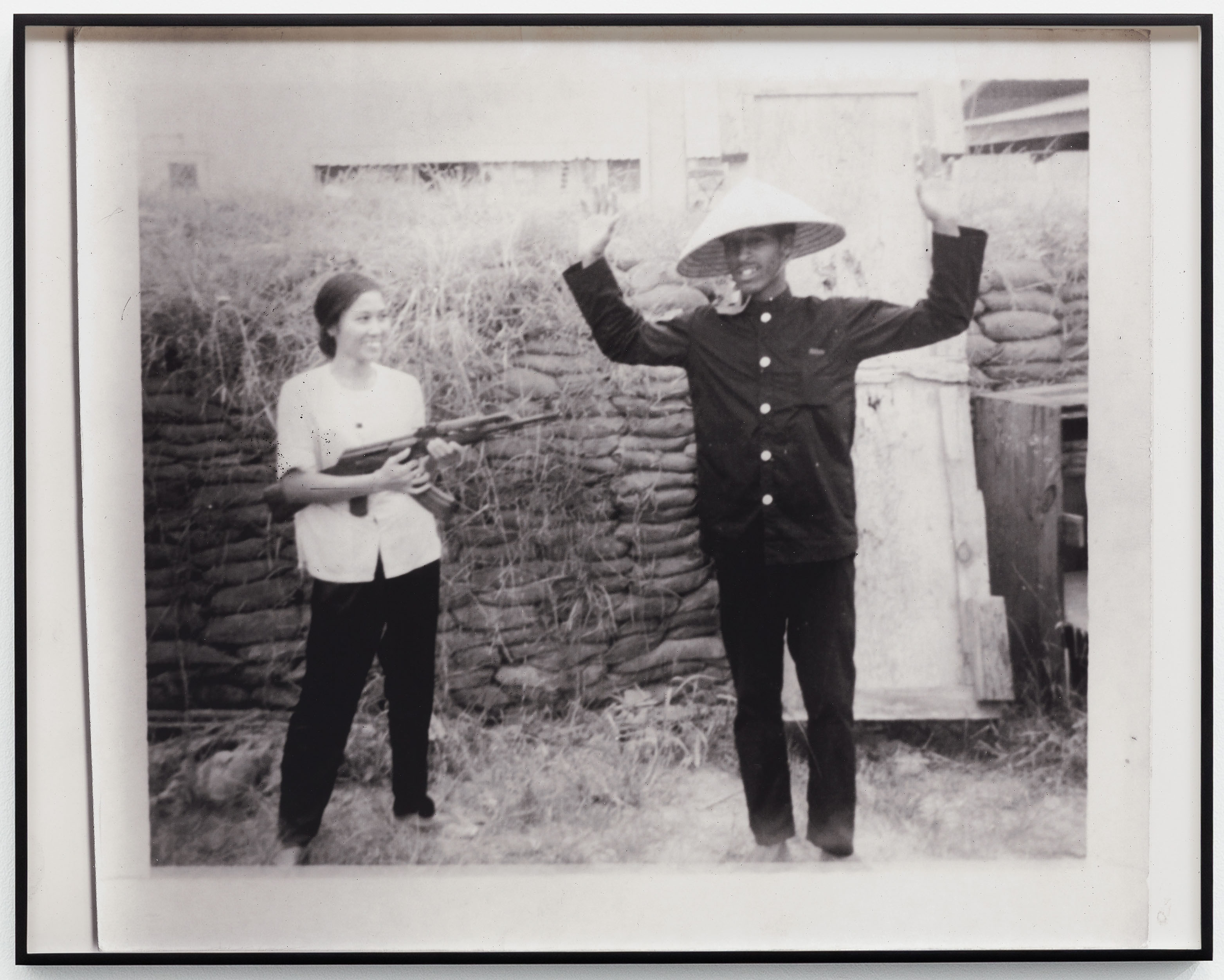 A woman smiling as she points a gun at a man with his hands in the air.