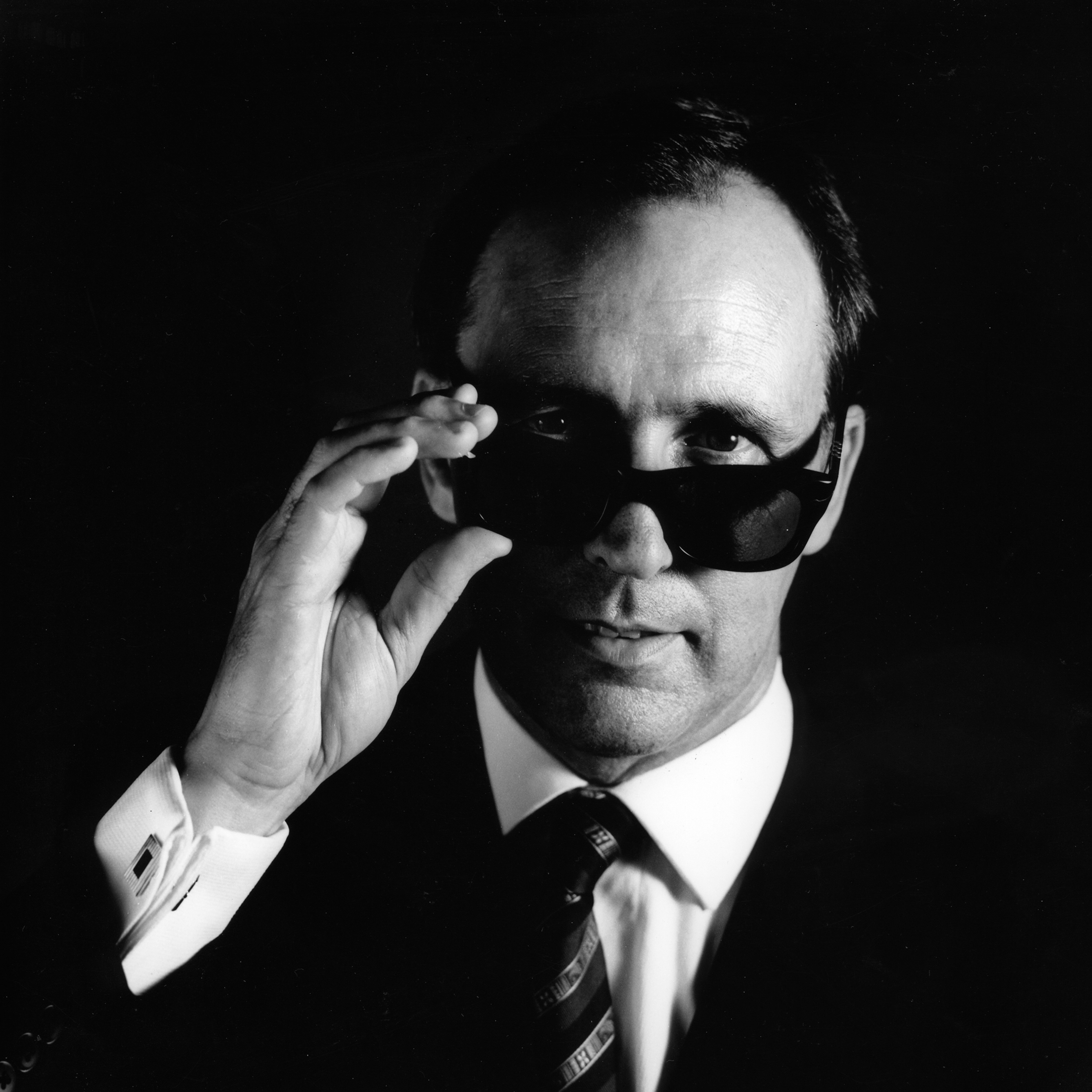 Black and white portrait image of Paul Keating, posing with a pair of sunglasses.