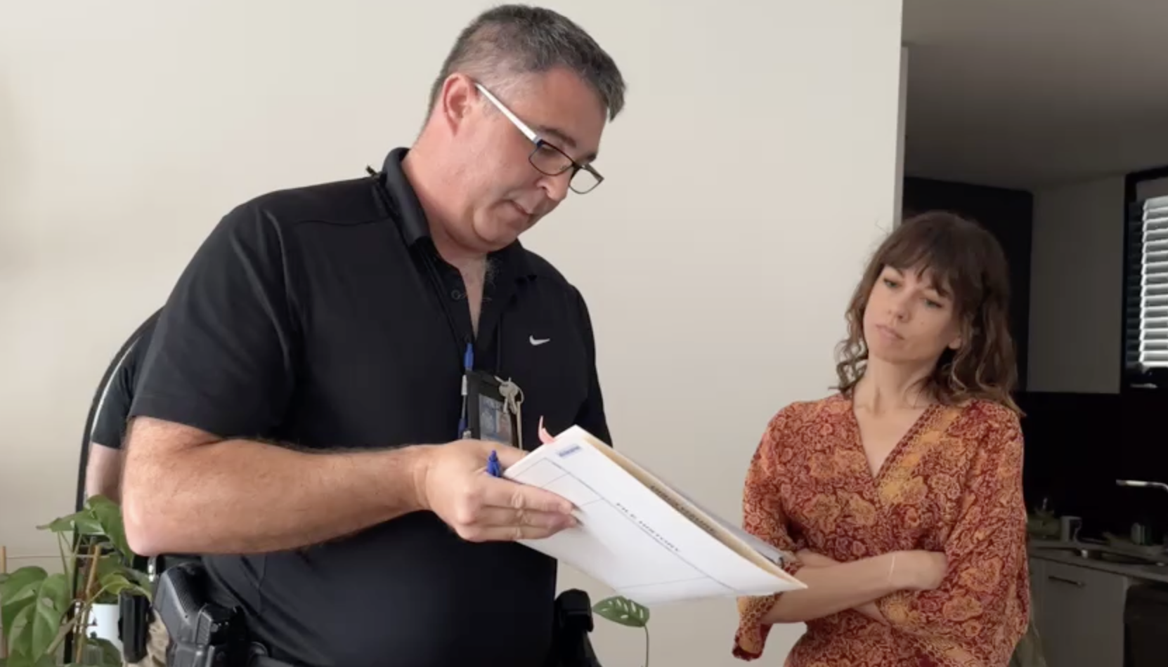 A police officer shows a document to a woman in a floral robe. 