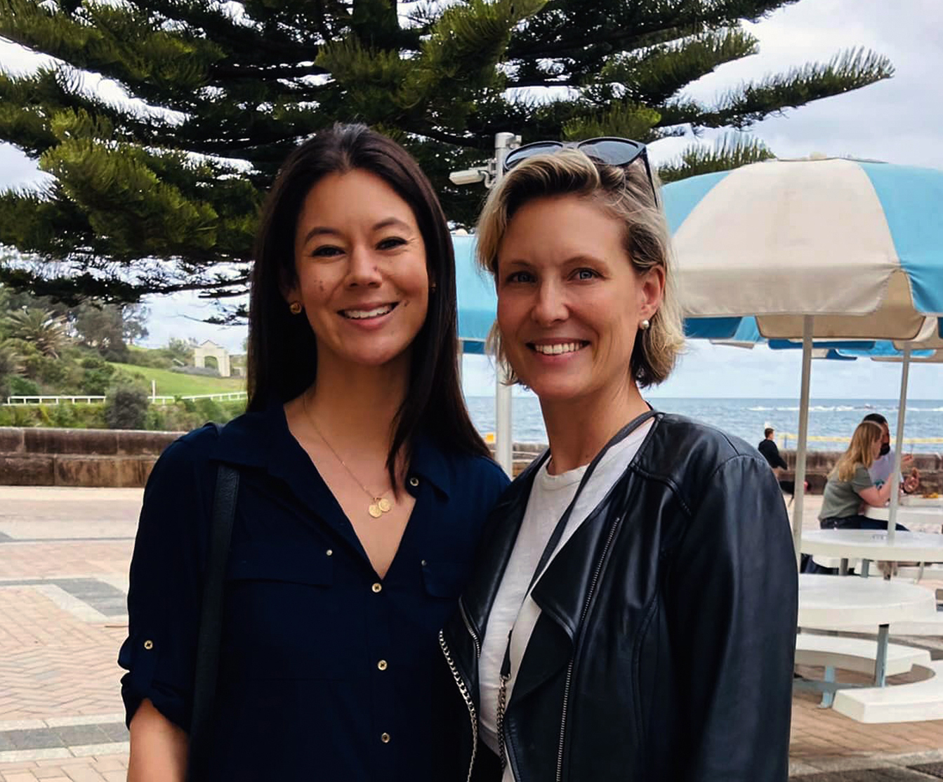 Two women smiling for the camera at a beach.