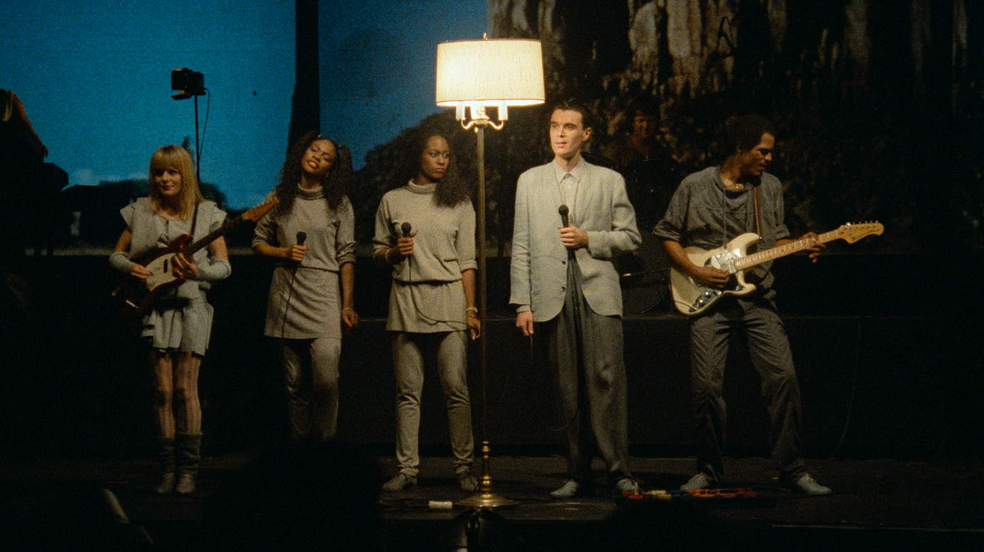 Musicians in grey clothing perform under a lamp on stage.