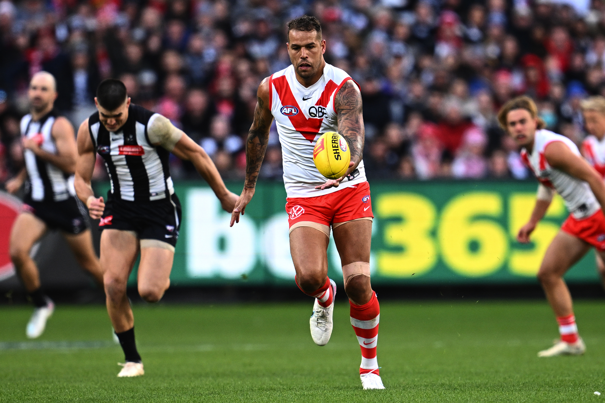 An AFL player in a white and red jersey runs with the ball, an opponent chasing behind him.