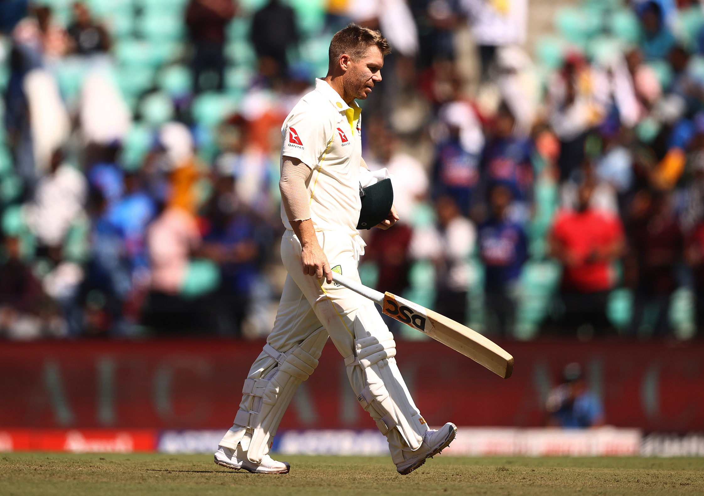 David Warner departs the cricket pitch, head slumped and carrying his cricket bat and helmet.