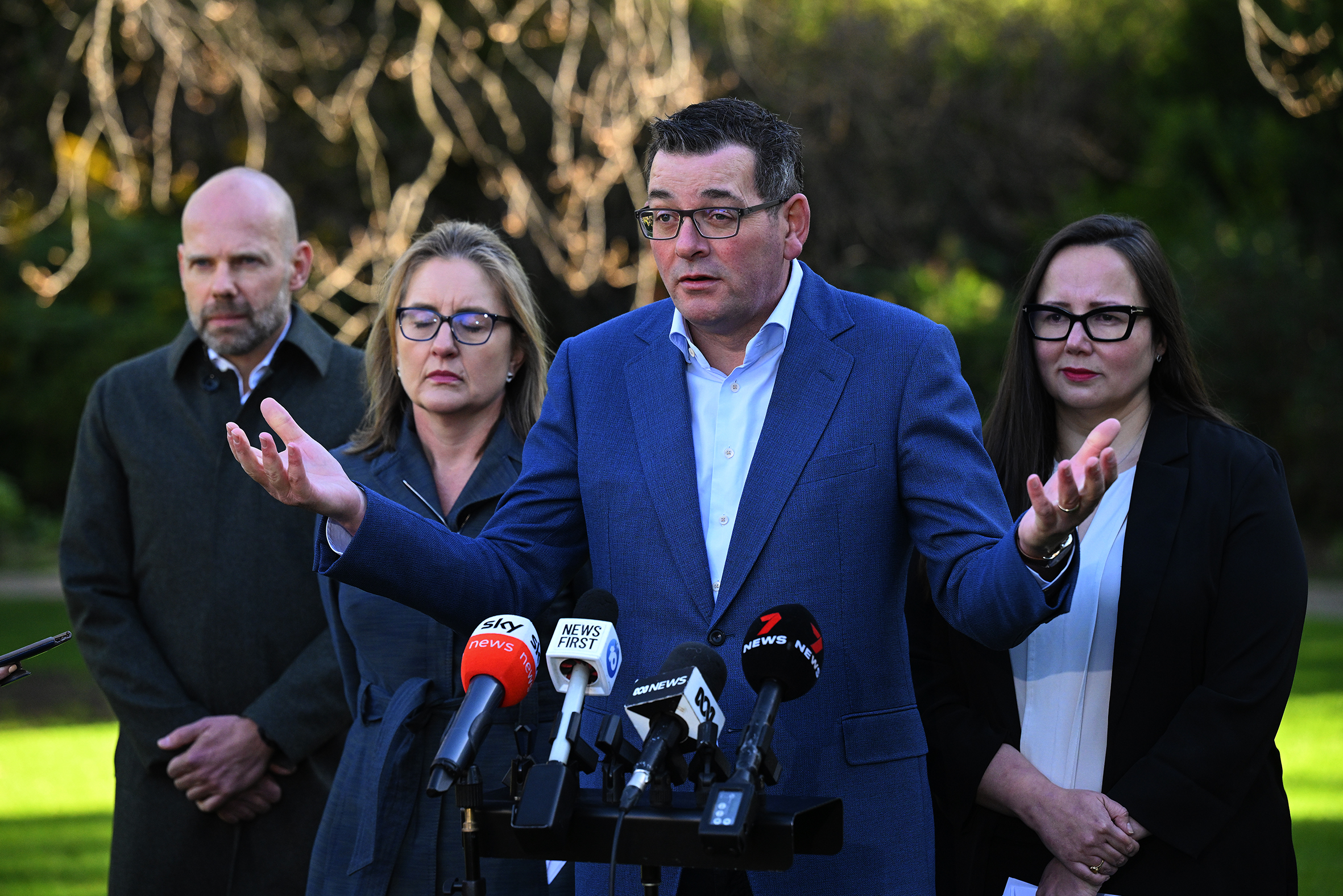 Politicians stand behind microphones on a field.
