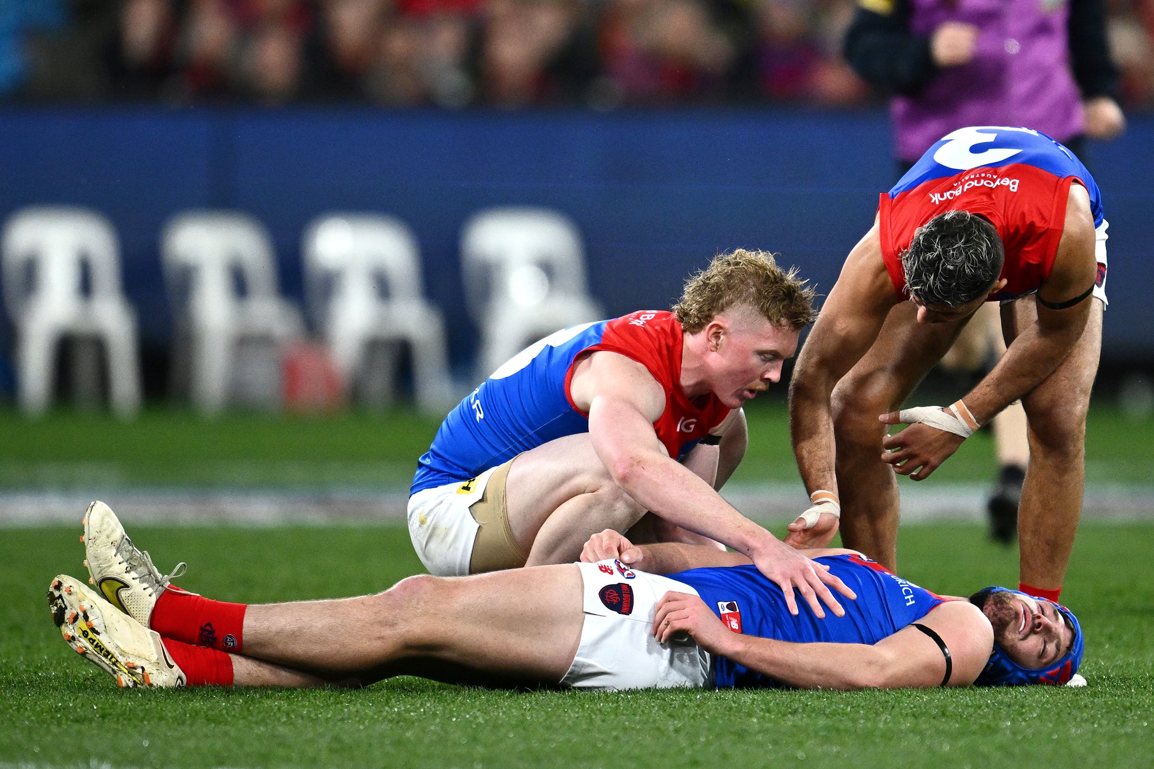 A pair of ALFL players check their teammate, who is sprawled unconscious on a football pitch.
