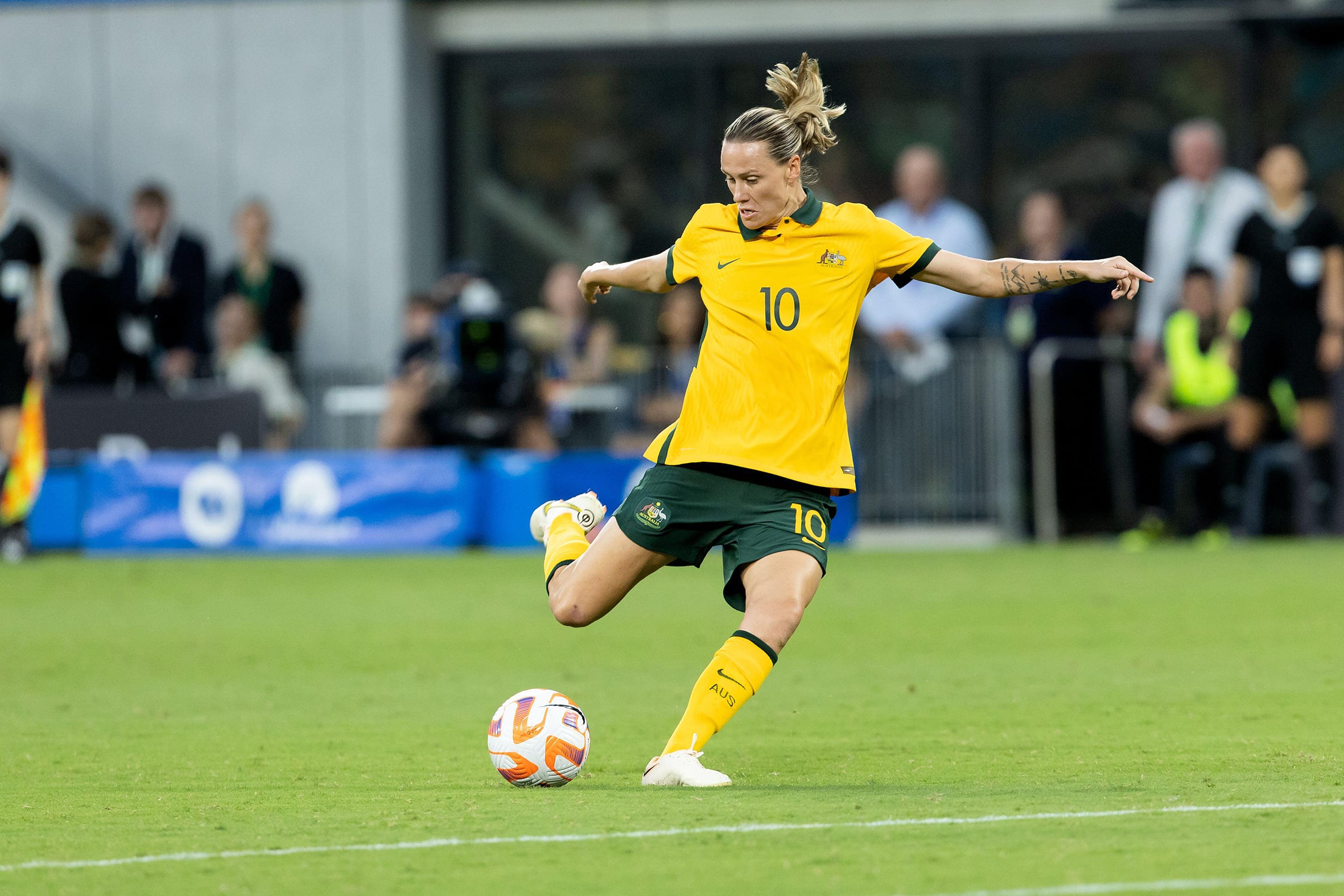 A soccer player in green and gold colours kicks a ball on the pitch.
