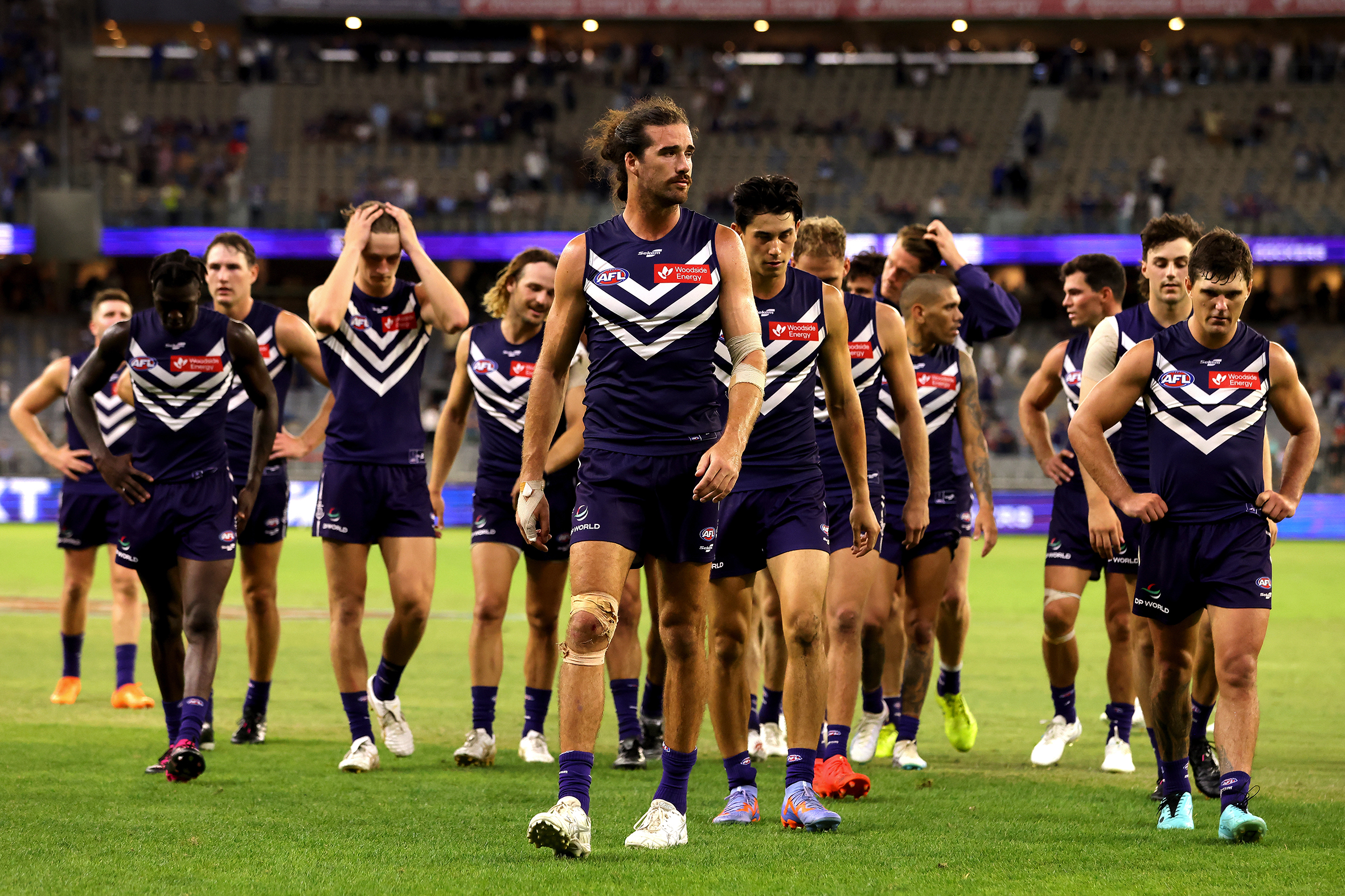 The Fremantle Dockers walking off the pitch in purple jerseys, a sparsely populated stand behind them.