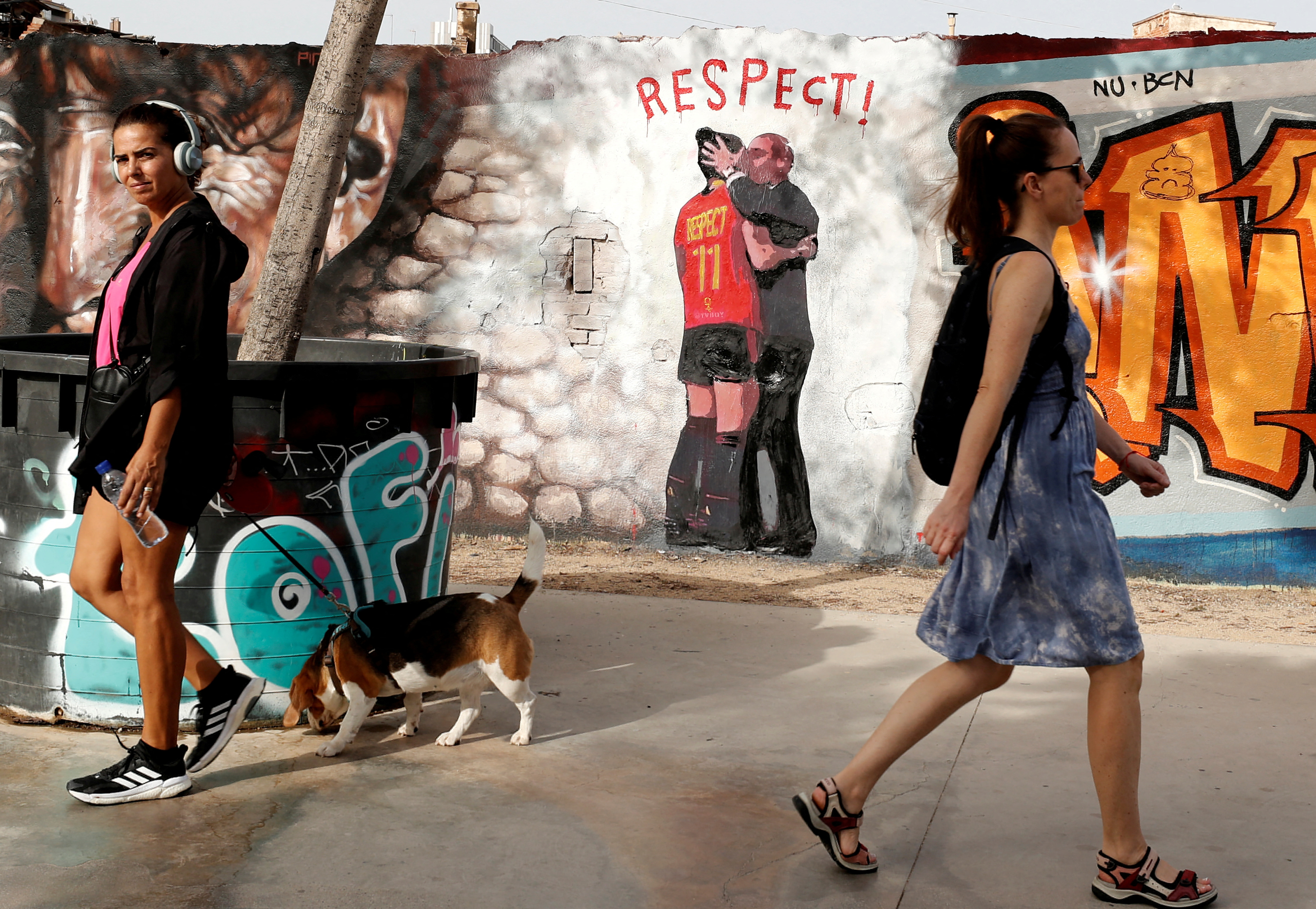 Women walk past a mural of a man in a suit kissing a woman in a spanish soccer uniform.