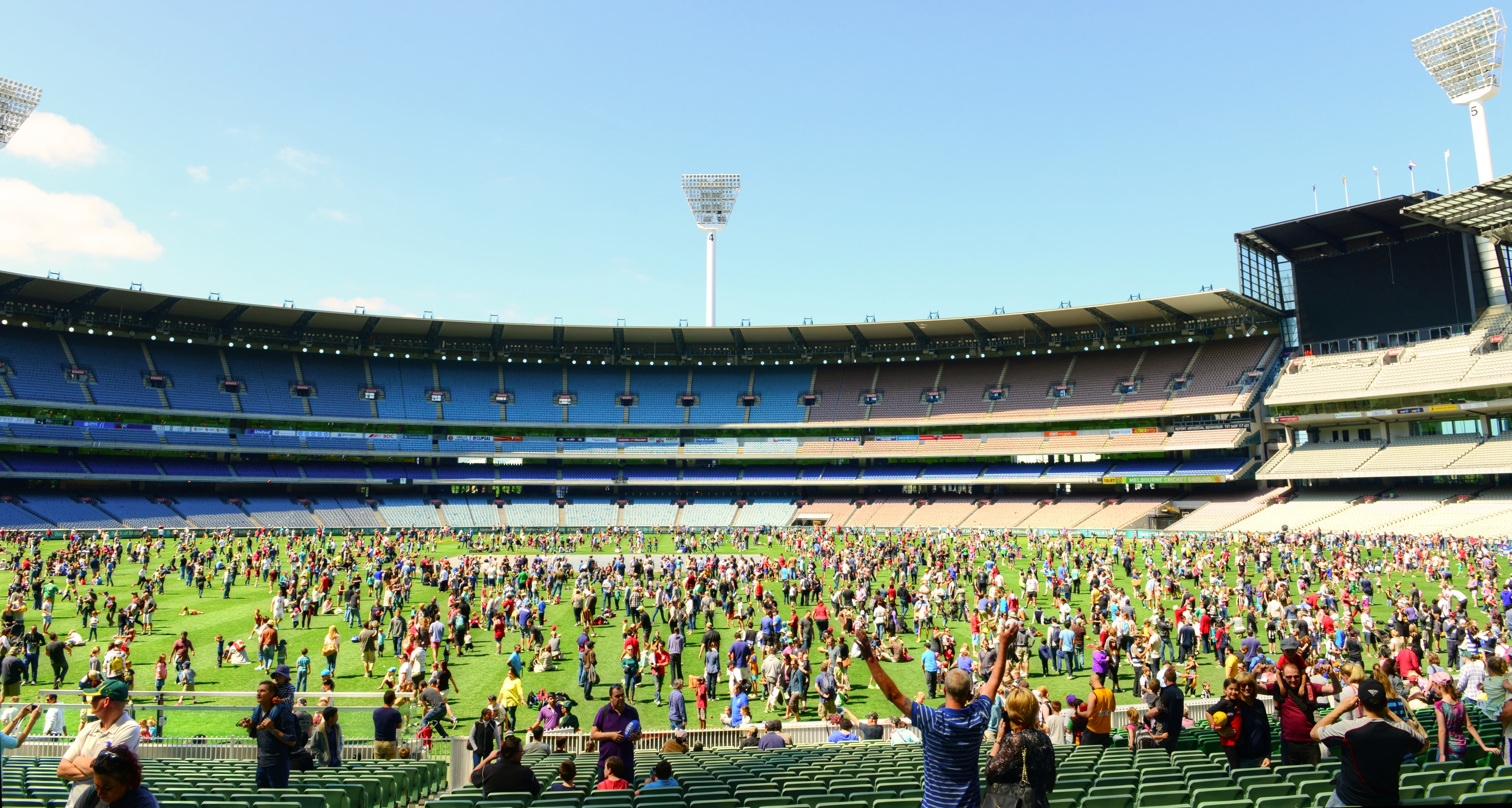 A crowd of people are scattered across the MCG, a blue sky above them.
