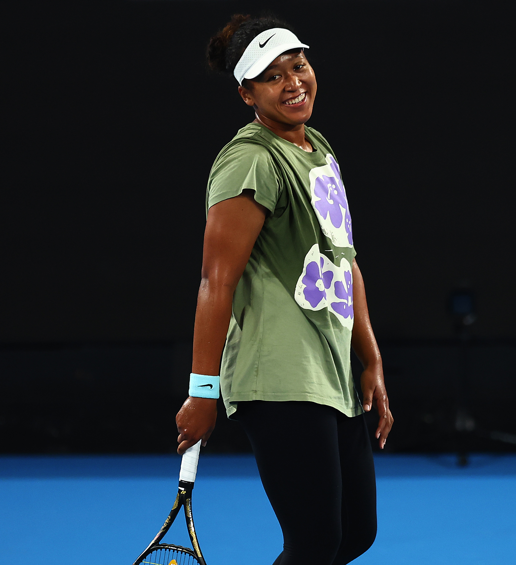 Naomi Osaka smiling on court with a racquet in her hand.