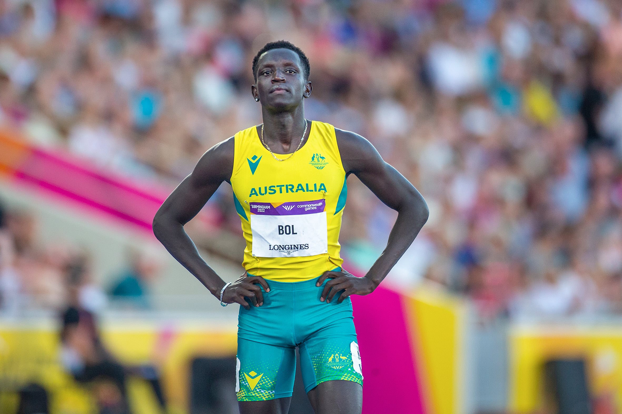 Runner Peter Bol on a race track with his hands on hips hips. He is wearing a green and gold Australia running outfit