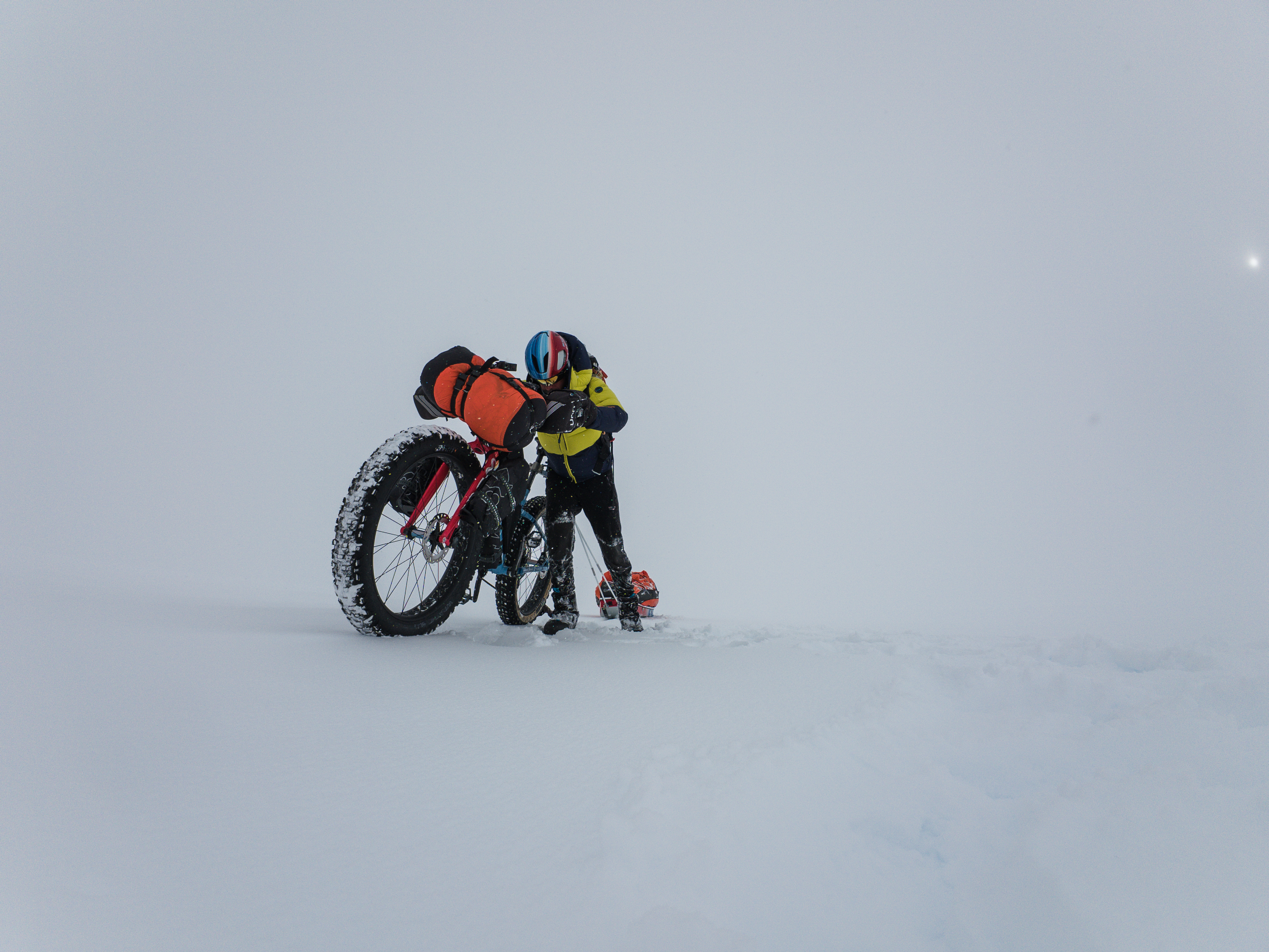 A man in snow gear pushing a bike through Antarctica.