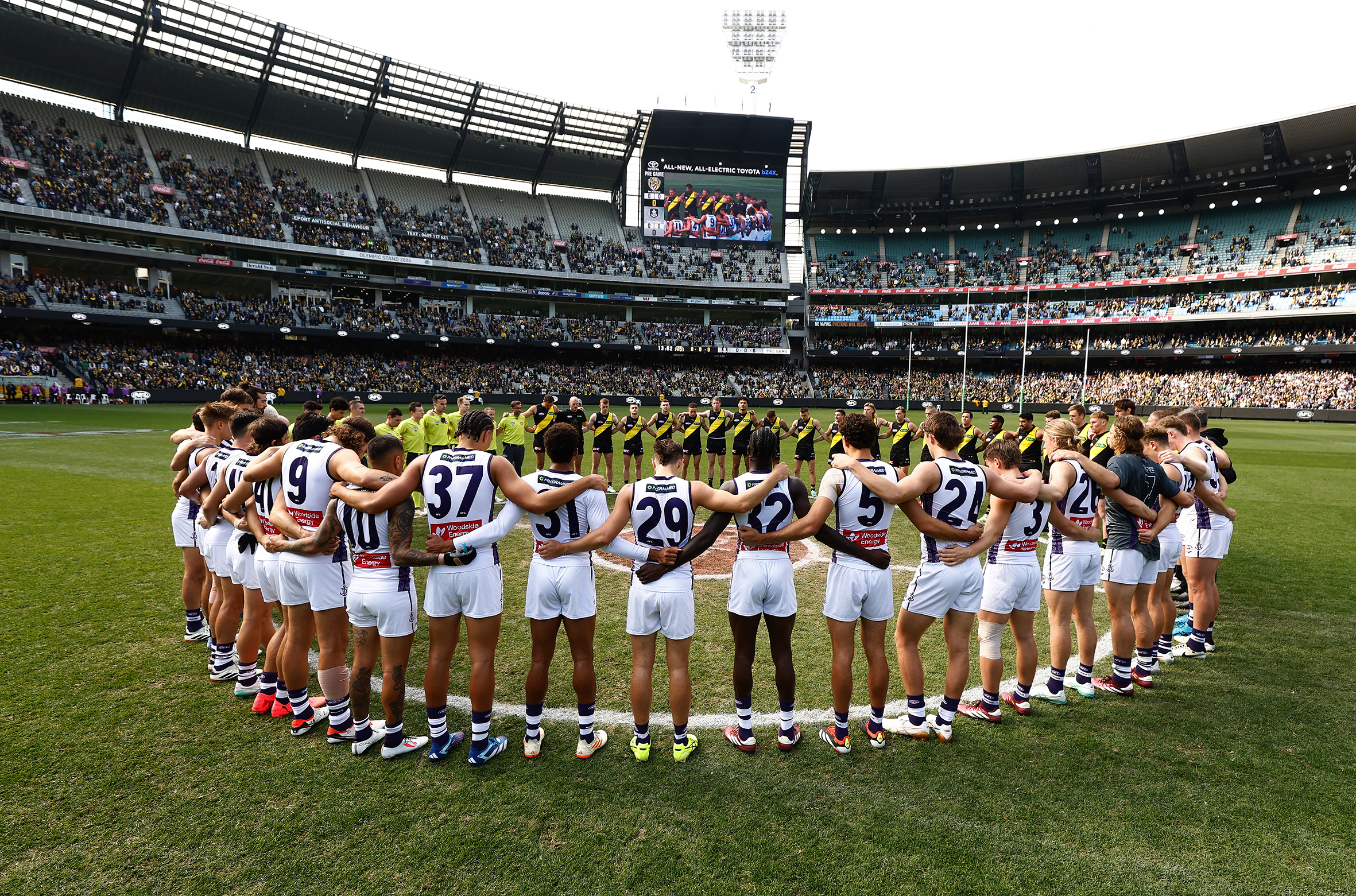 Richmond and Fremantle players, coaches and umpires form a circle as a show of support against gender-based violence