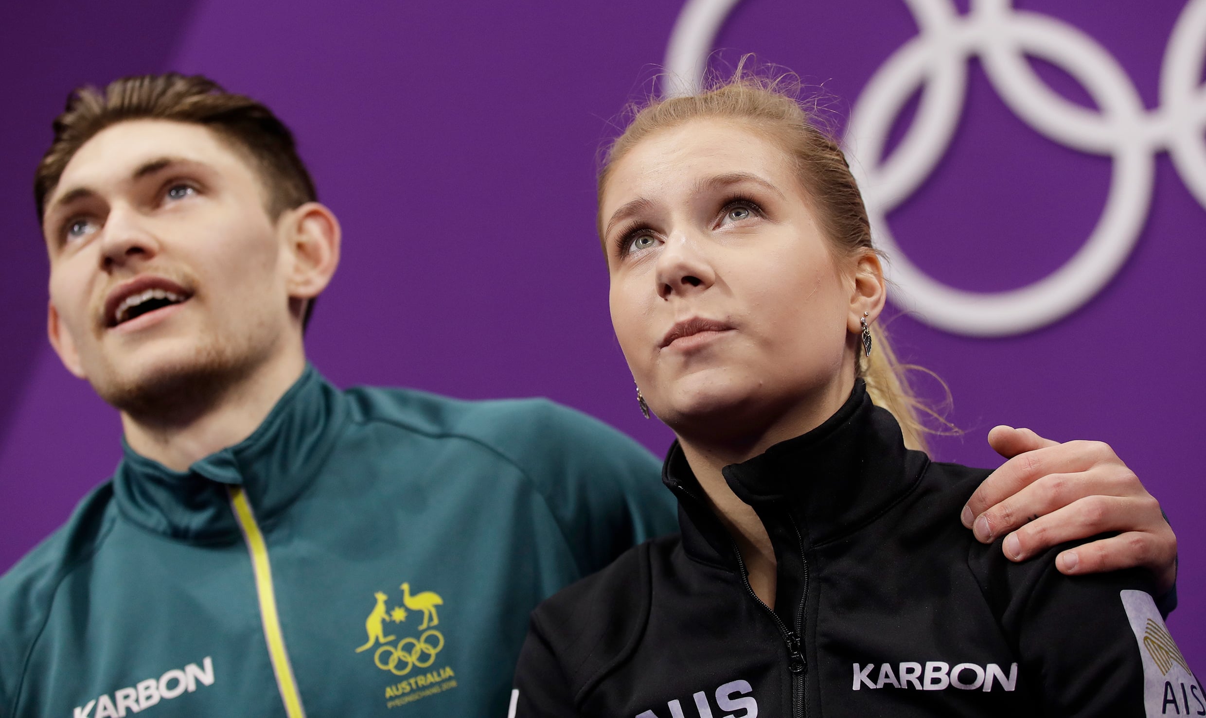 Two young Caucasian people in athletic gear look up towards the top of the image; their faces are hopeful and apprehensive.