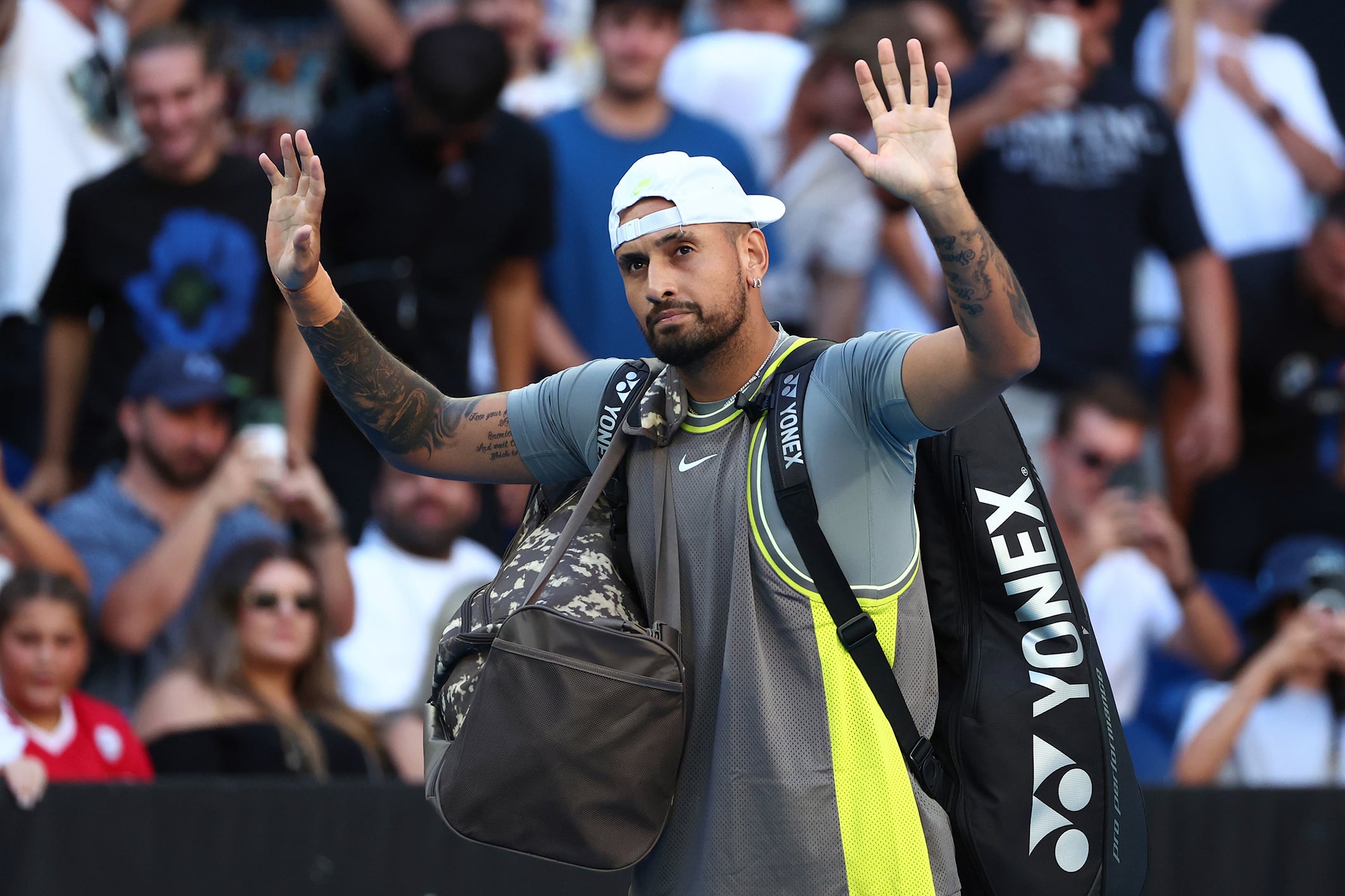 Nick Kyrgios waves to the crowd while walking off the tennis court.