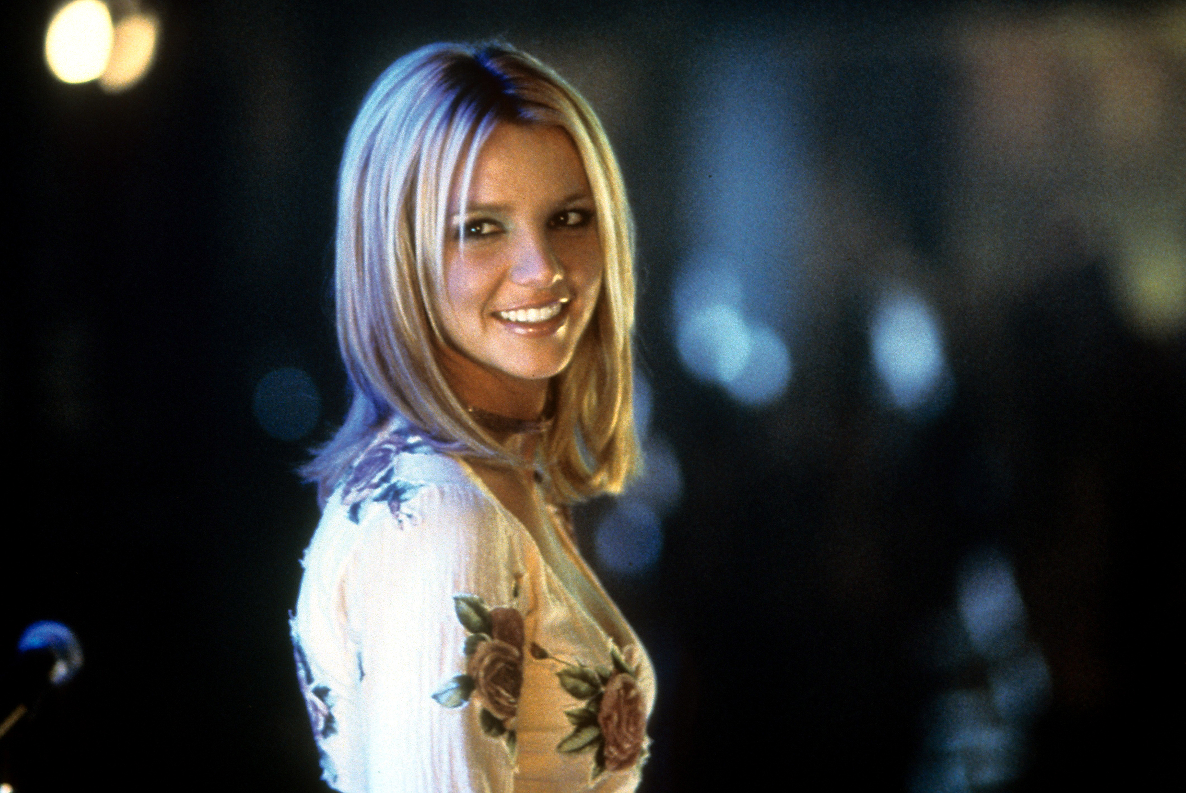 Britney Spears wearing a floral dress. The lights in the night are out of focus behind her.