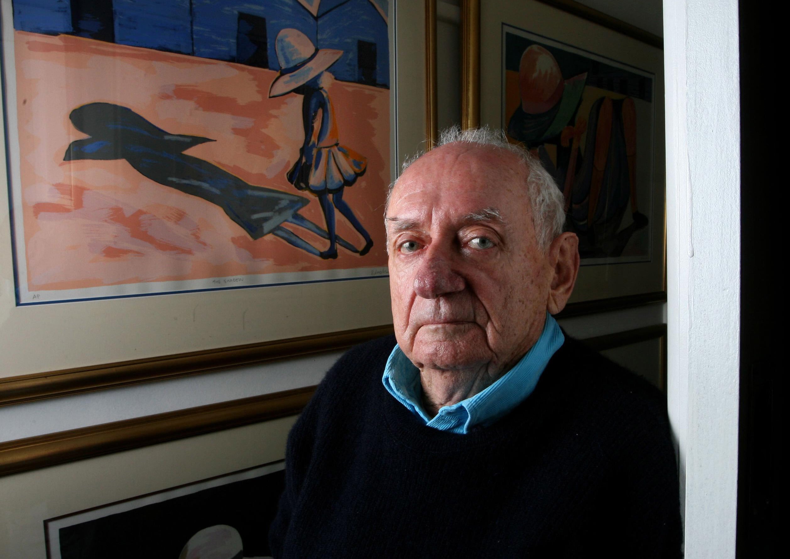 An elderly man standing beside a painting of a young girl.