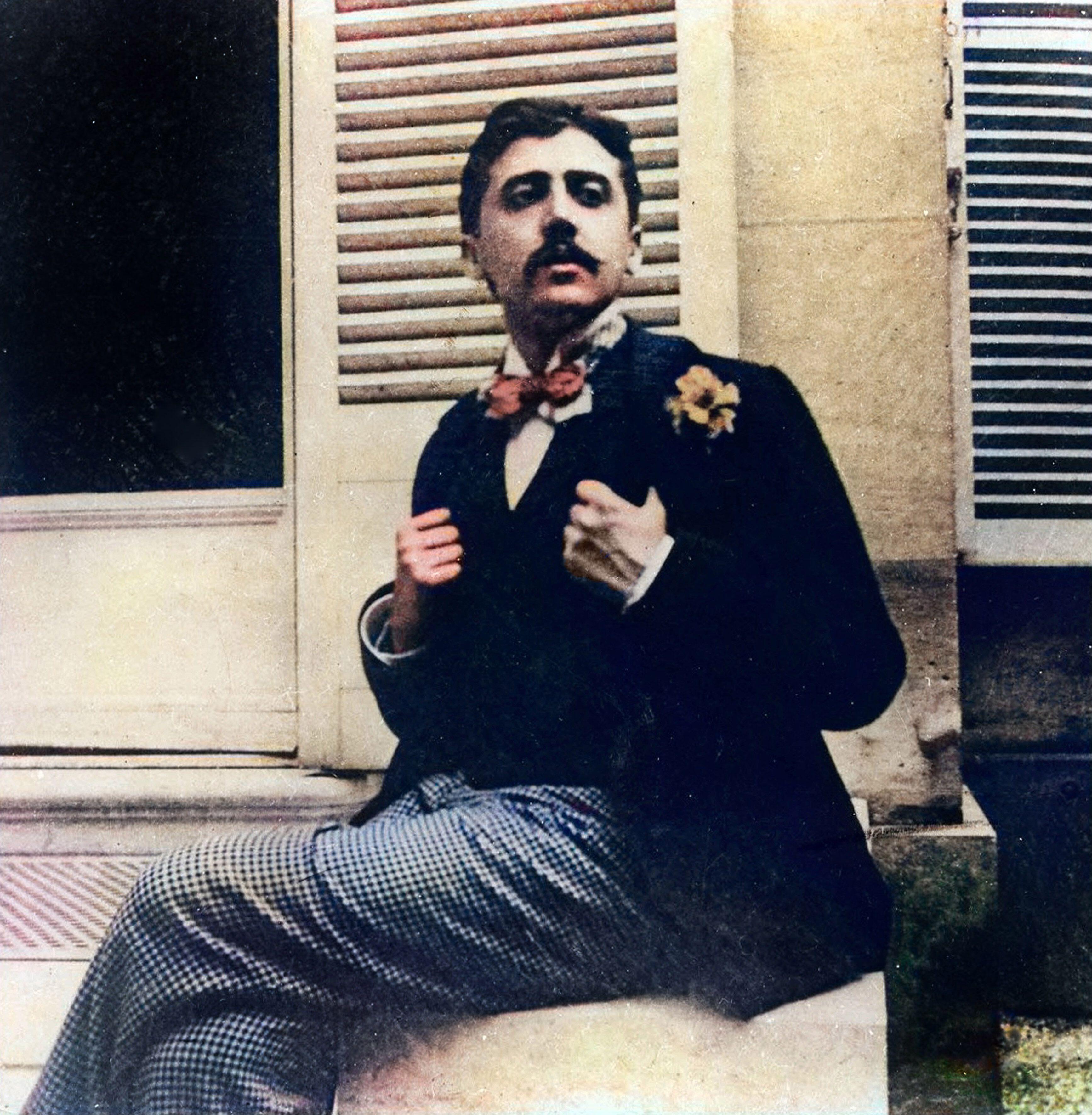 A grainy photograph of a man with a dark hair and a thick moustache matched with formal clothing and a red bowtie.