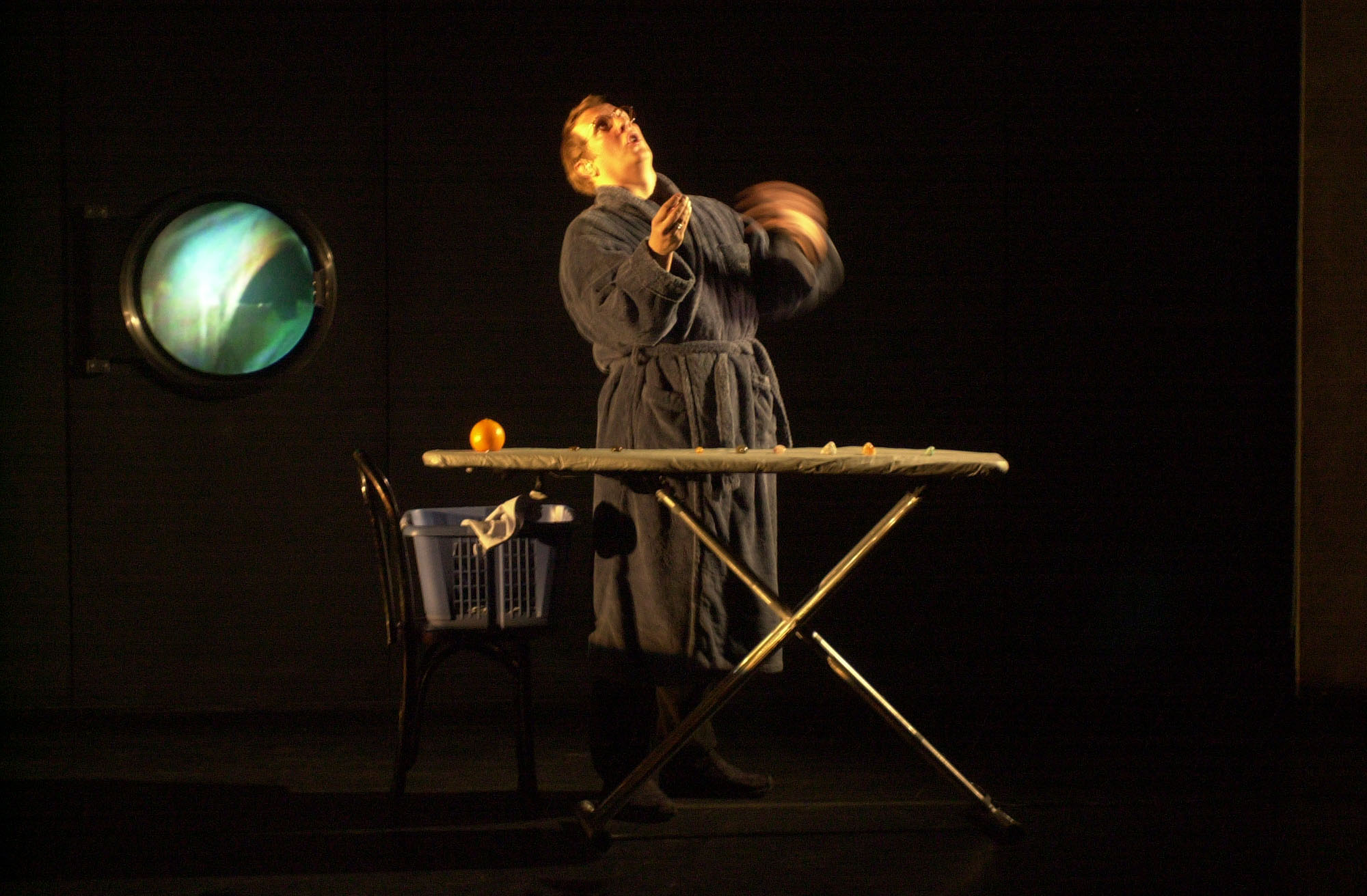A performer on stage in a a dressing gown. Eyes are fixated above as they stand beside an ironing board.