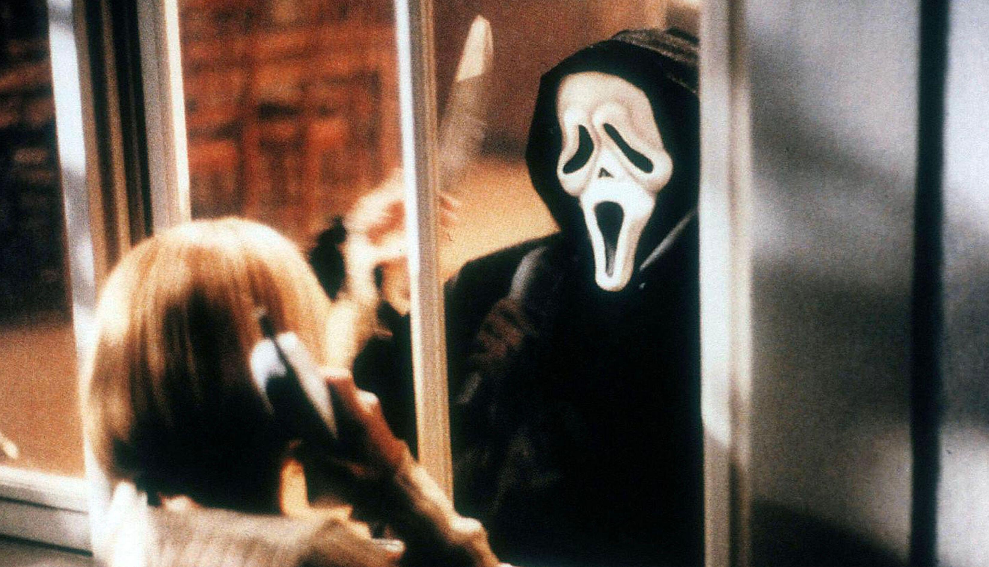 A figure in a cloak and white mask has a knife raised in one hand, directed towards a woman who is speaking on the telephone. A sliding door acts as a partial obstruction between them.