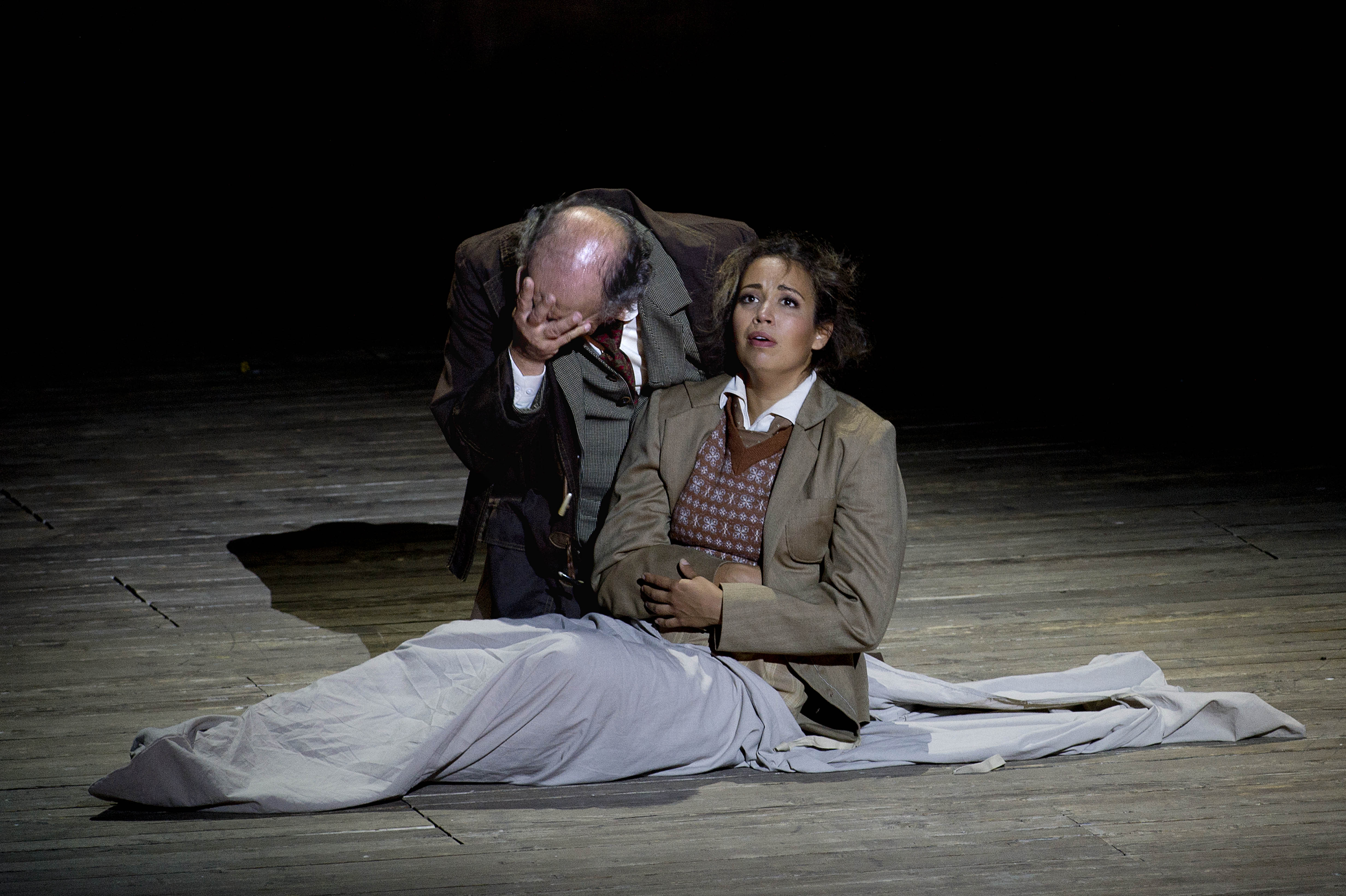 Main image: A man and a woman sit on a wooden stage, wearing 1950s style clothing. The man is older and going bald, and holds his face in his hand as if he is distressed. The woman is looking up to the left with an expression of awe. Inset image: A well-lit portrait of a pretty Caucasian woman with glossy brown hair smiling at the camera.