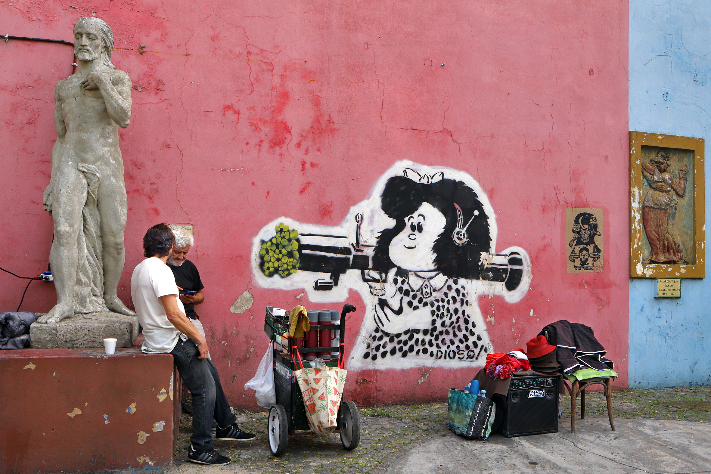 Two men beside a pink wall with graffiti.