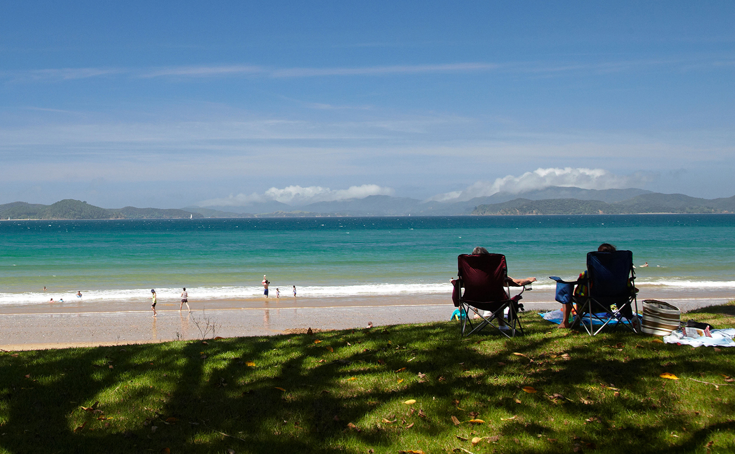 Two people sit in camping chairs overlooking the ocean.
