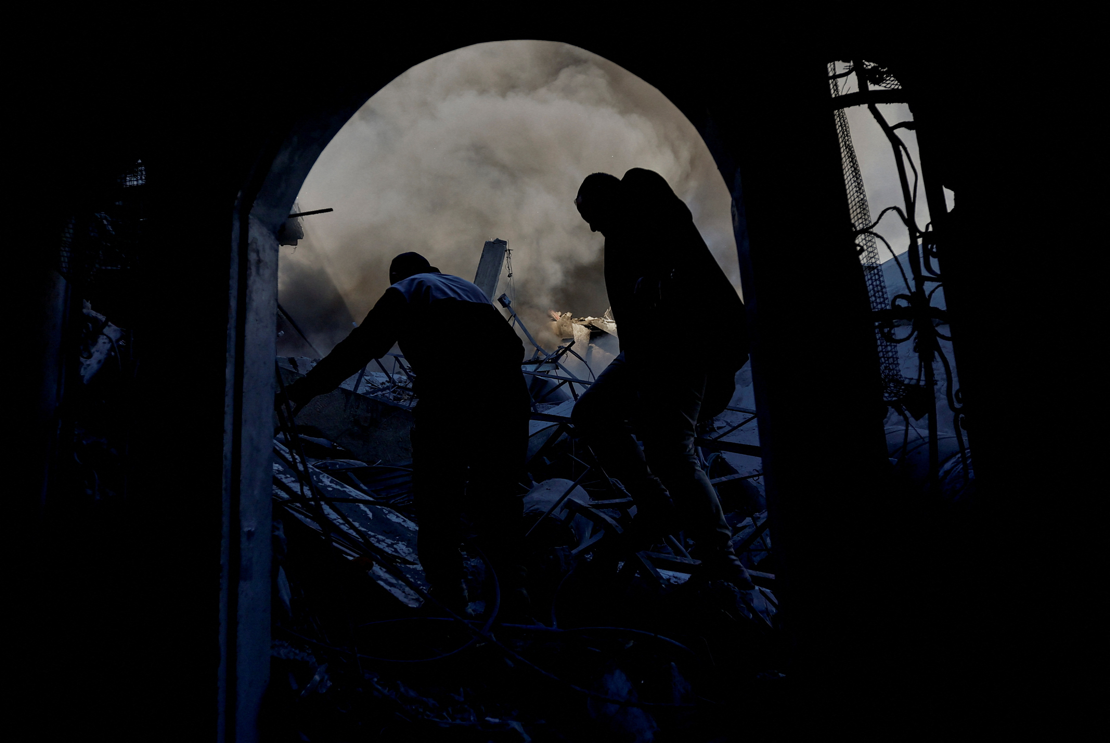 Two men walk through the rubble of a building in the dark.