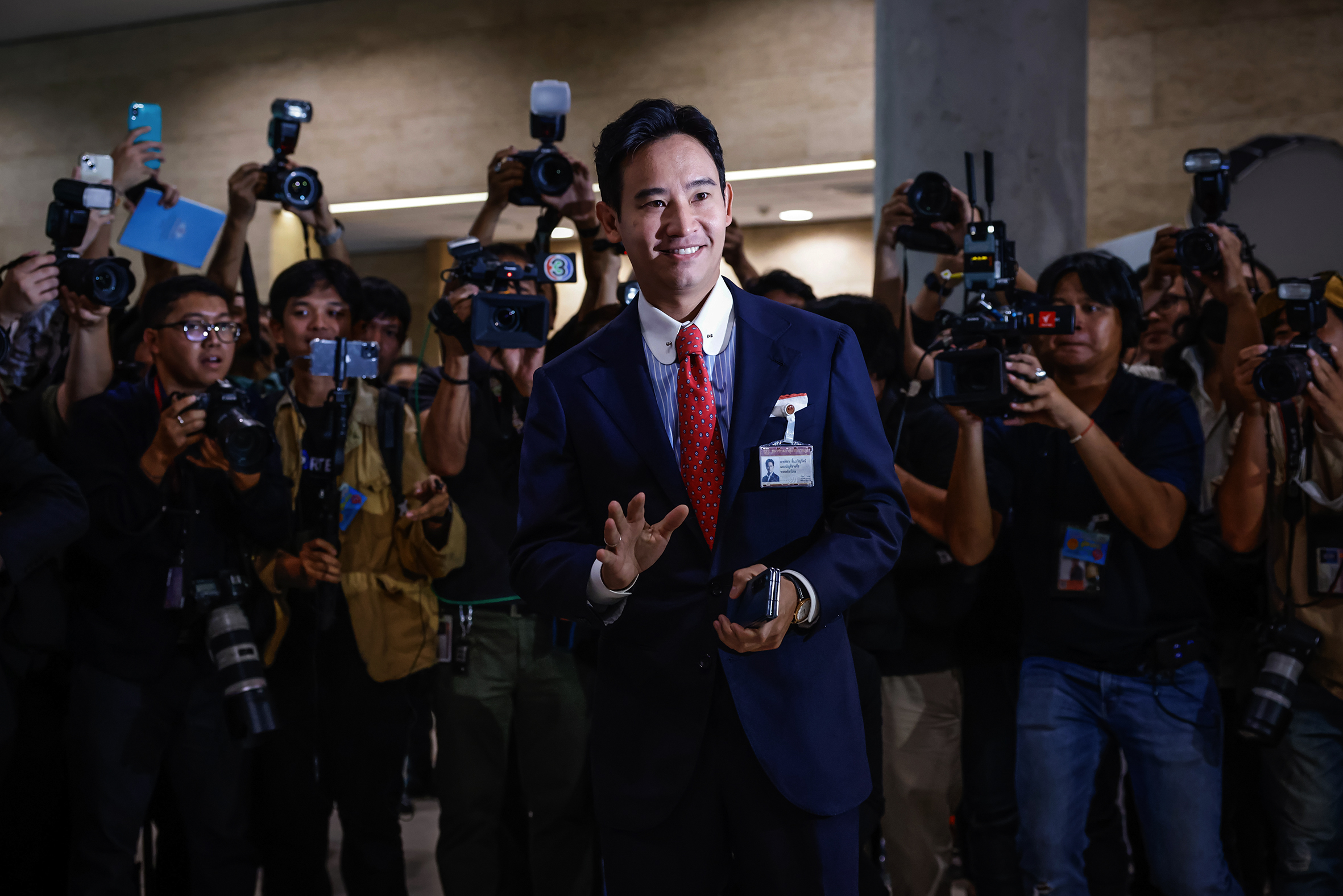 A politician in a suit surrounded by cameramen.