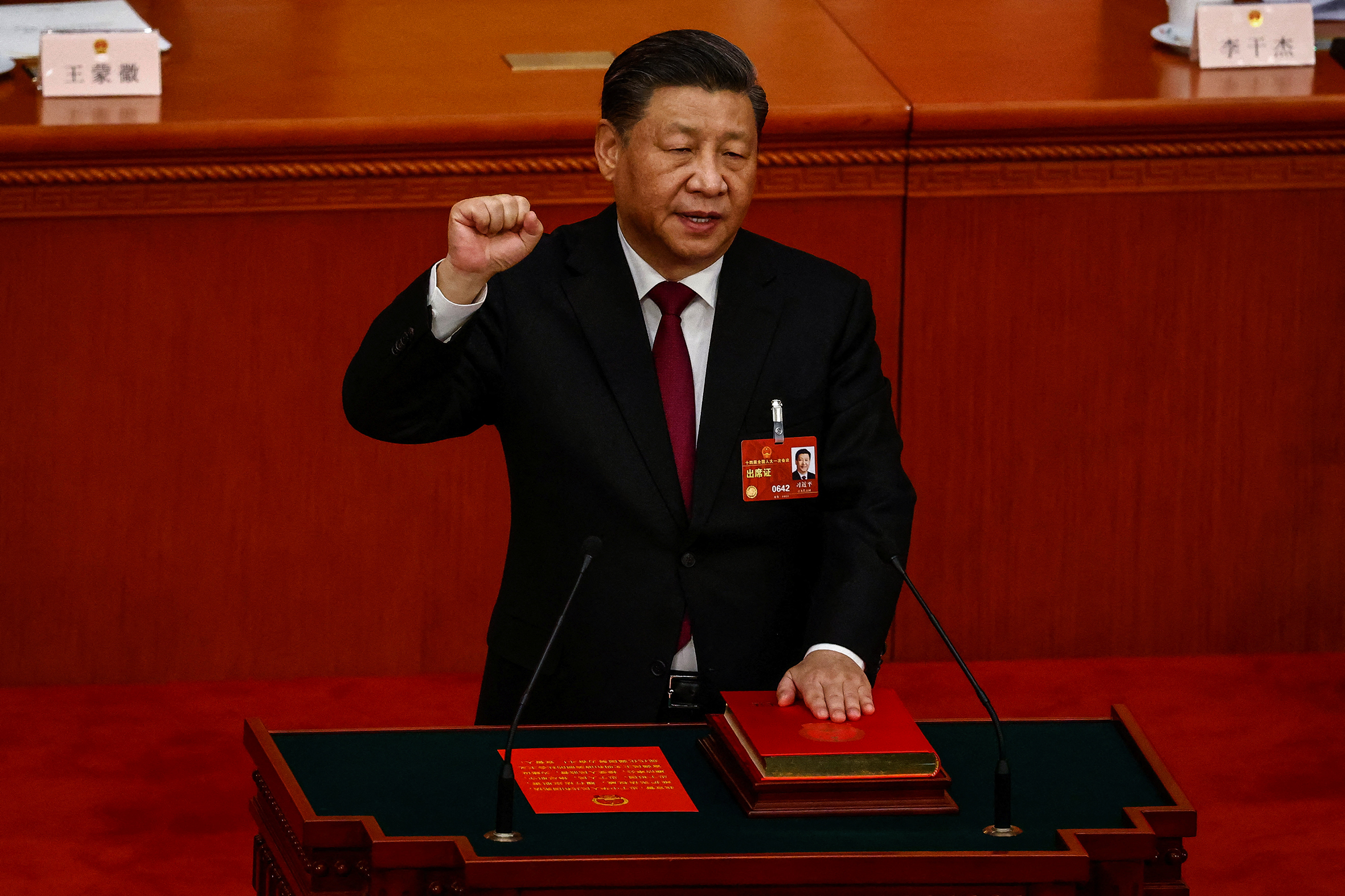 The president of China, Xi Jinping dressed in a suit with a name tag attached. He has a hand raised while the other rests on a book, swearing an oath.