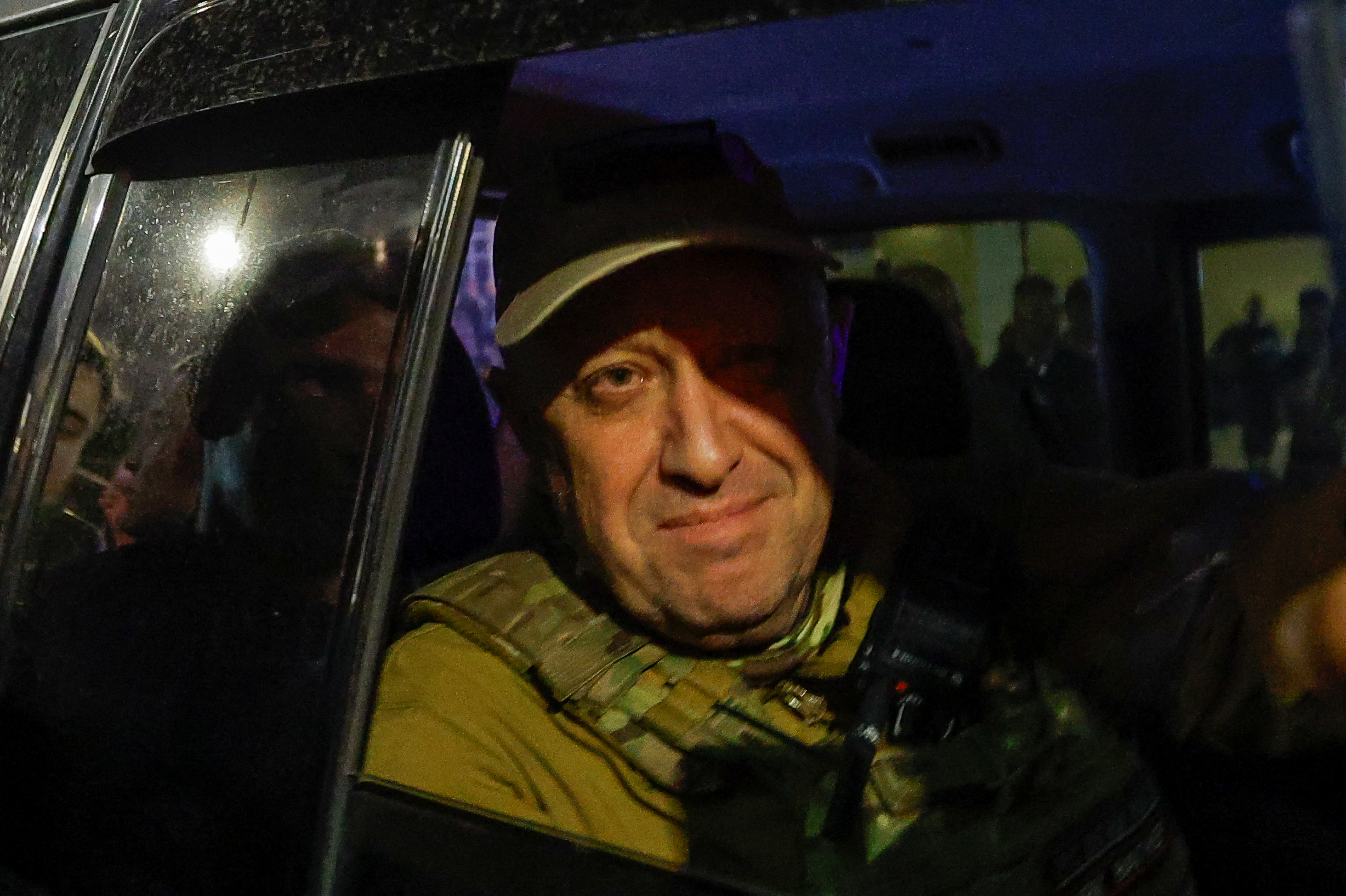 A middle-aged man dressed in a camo outfit sits in the back of a car with the window down.