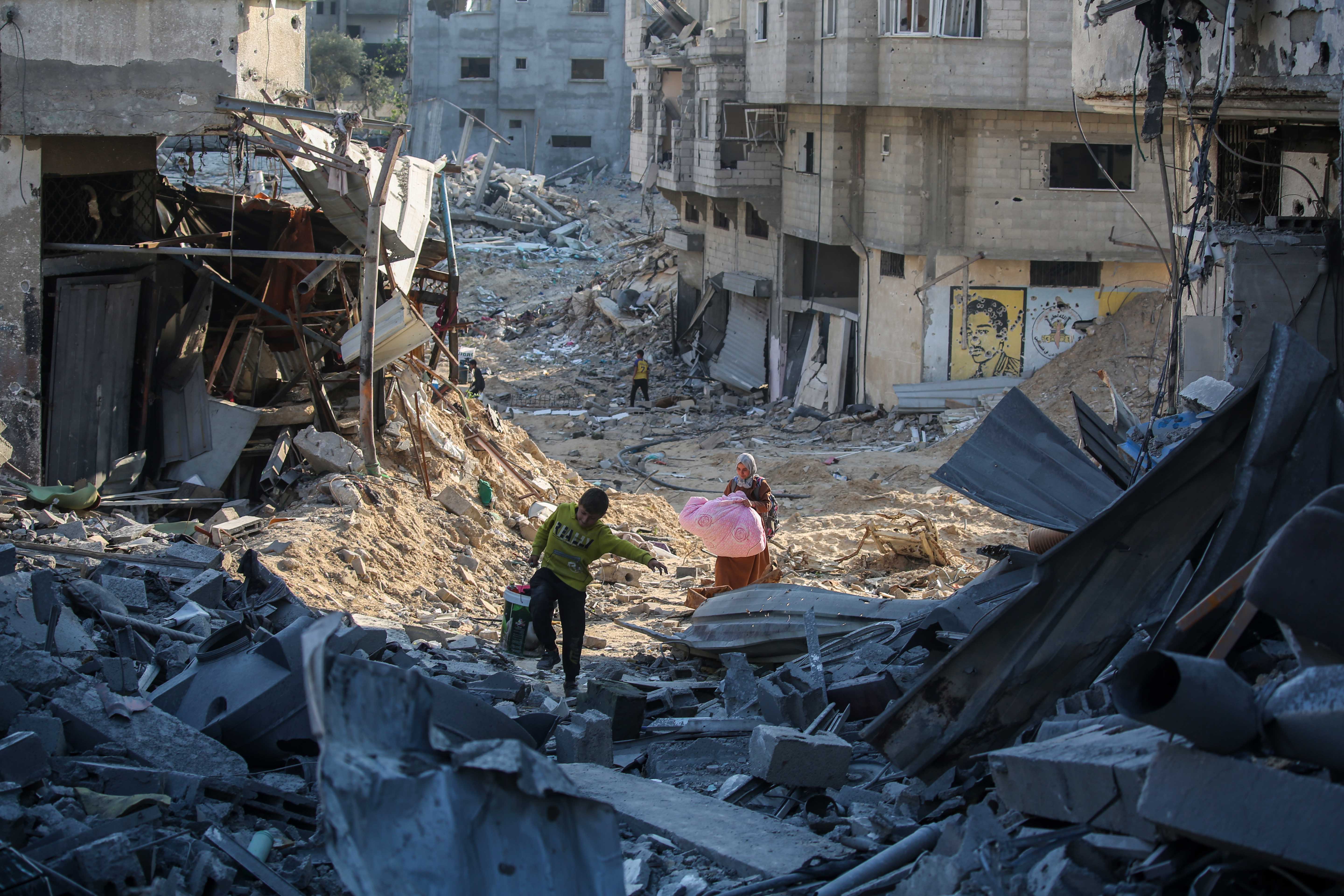 Palestinians carry their belongings through debris.