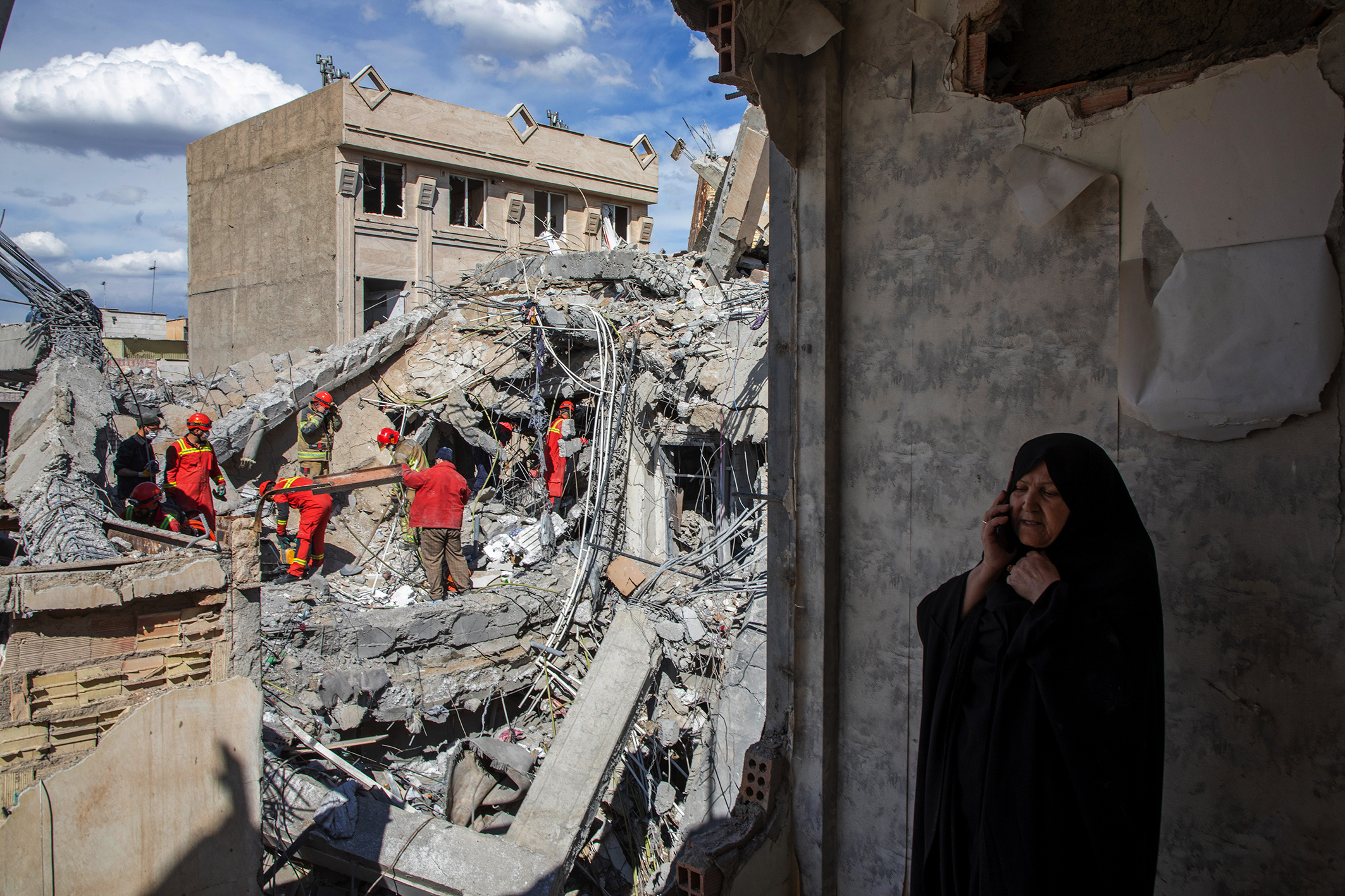 A Tehran resident makes a phone call as emergency workers sift through the rubble of a residential building hit in a recent air strike.