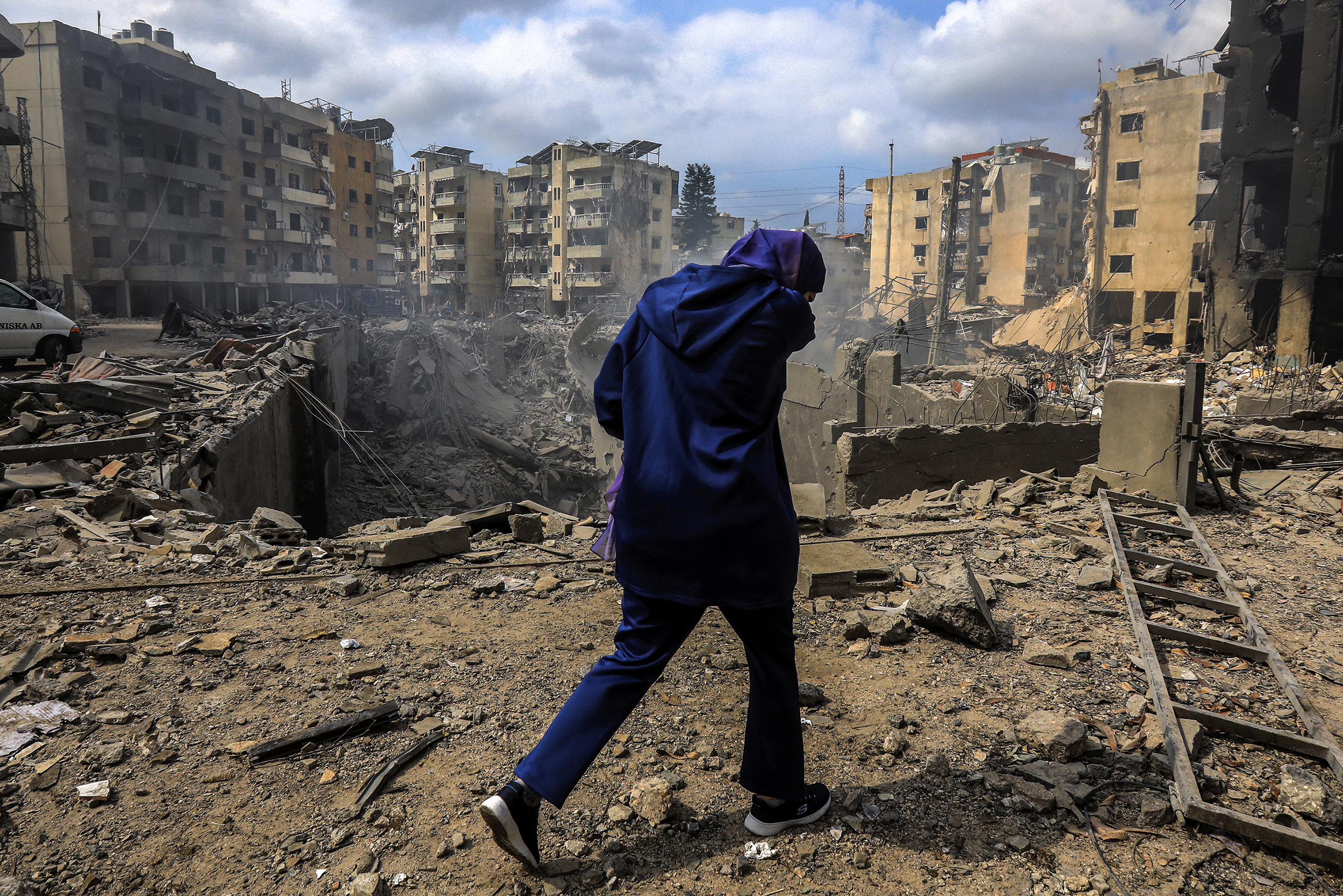 A woman passes the crater left by an Israeli air strike, debris all around her.