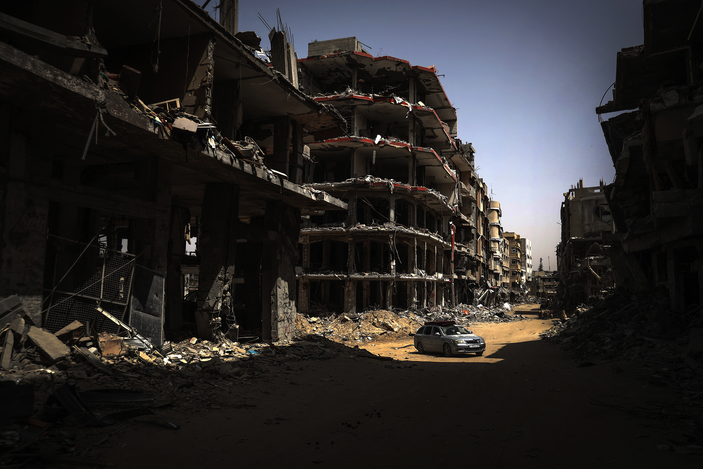 A car on a dirt road surrounded by destroyed buildings.